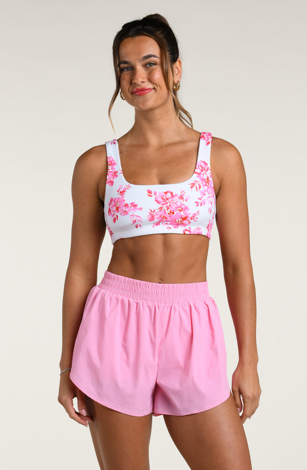 Woman wearing a pink floral sports bra and pink running shorts set on a white background
