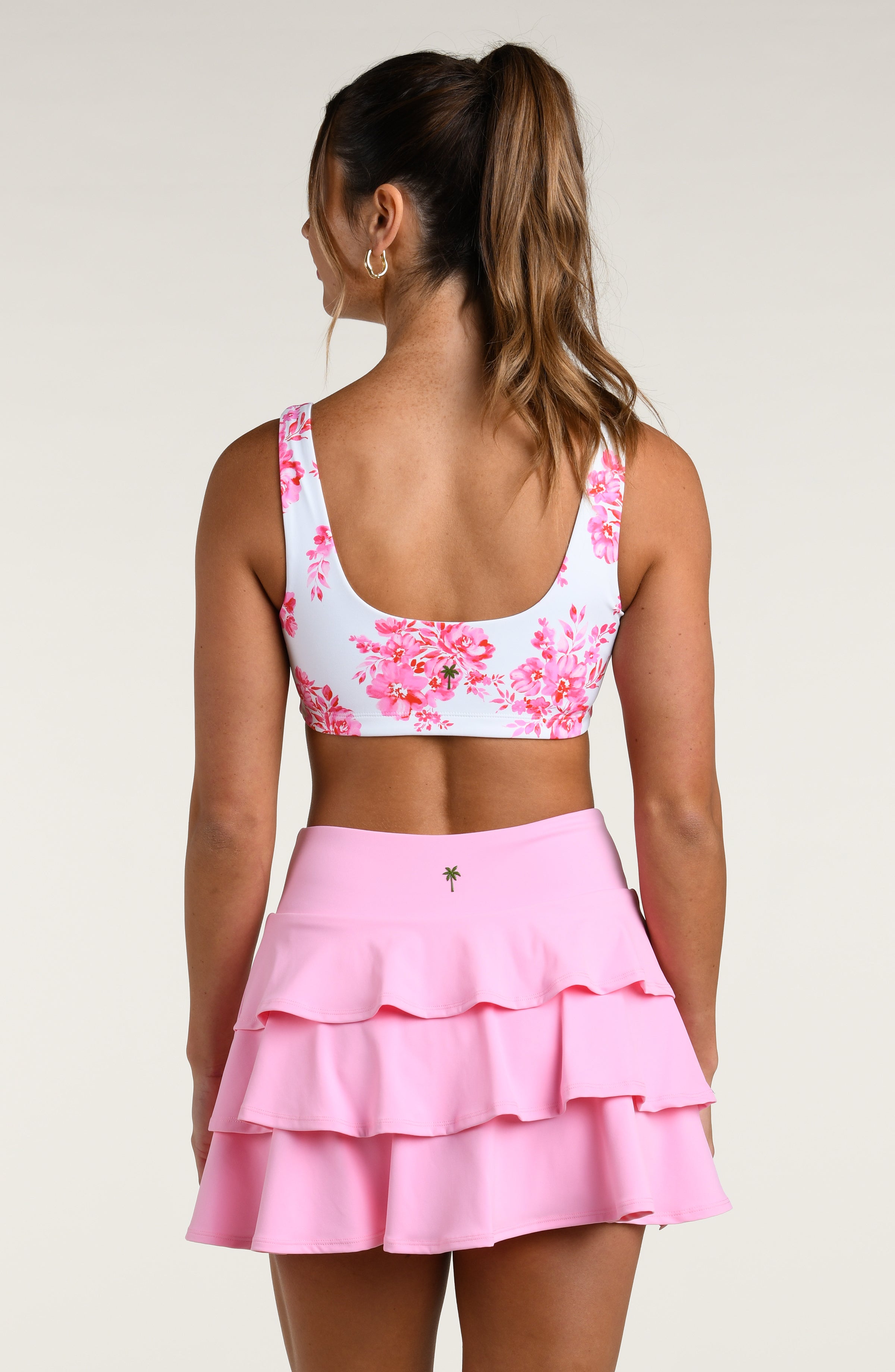 Woman wearing a pink floral sports bra and pink skort set on a white background