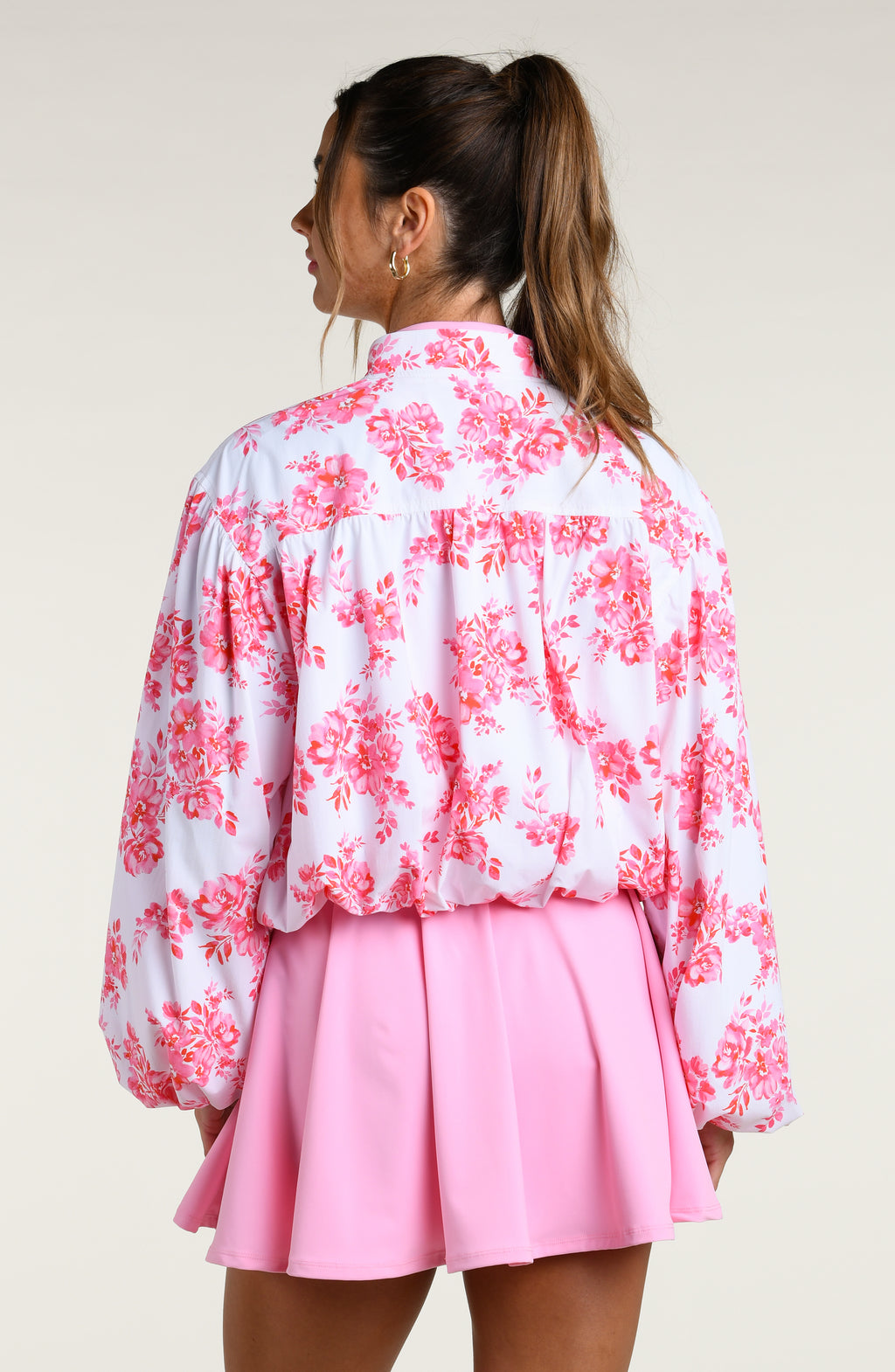 Woman wearing a pink floral jacket and pink tennis dress on a white background