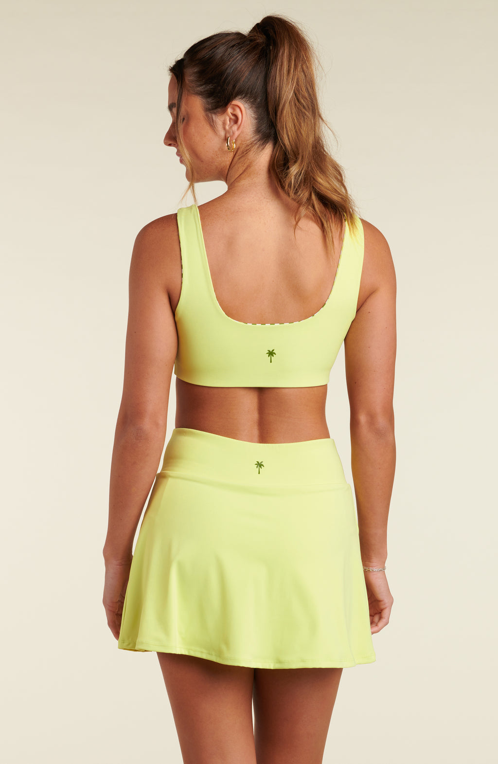 Woman wearing a bright yellow sports bra and matching skort on a beige background