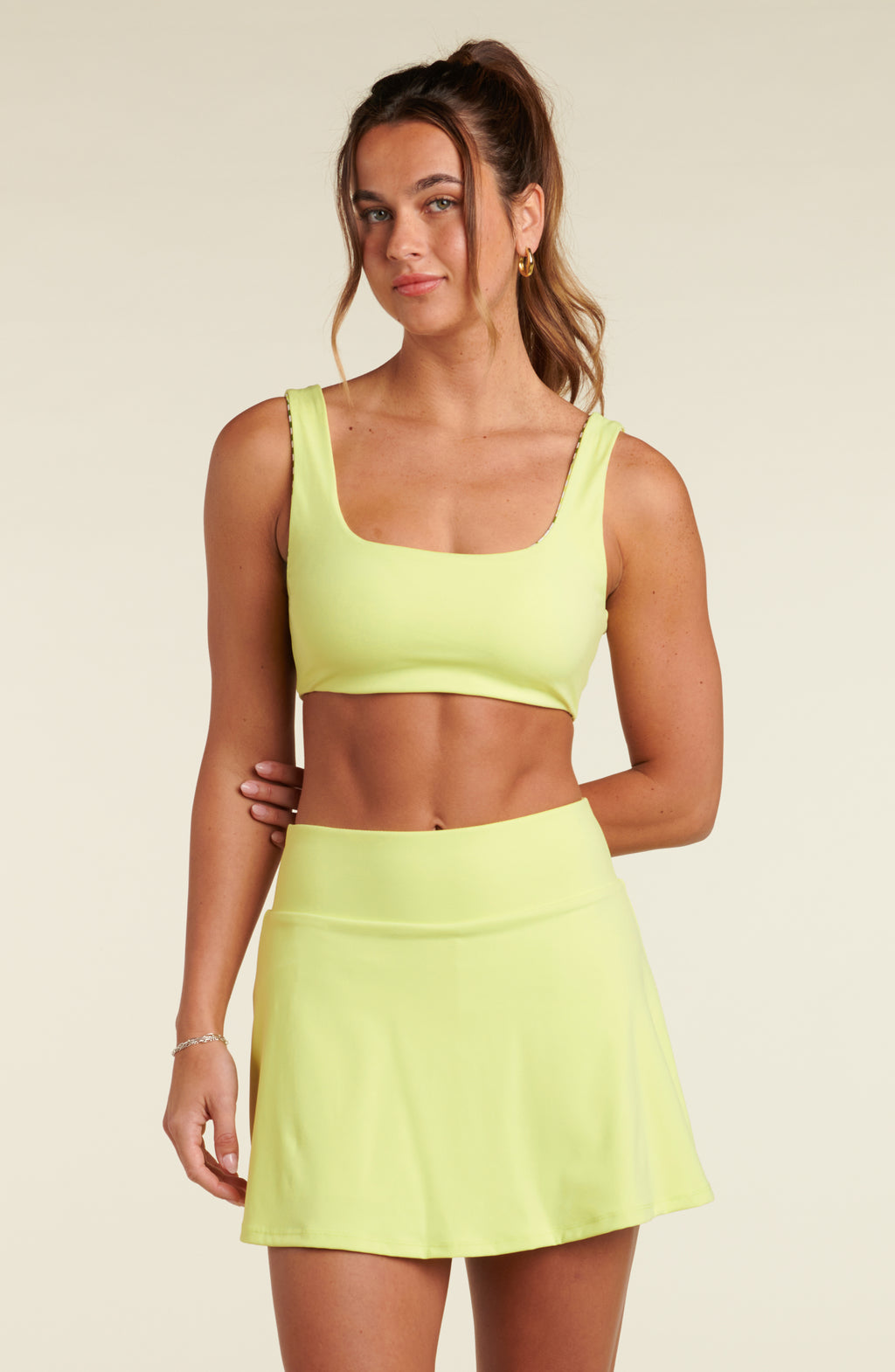 Woman wearing a lime green sports bra and matching swim skort against a white background.