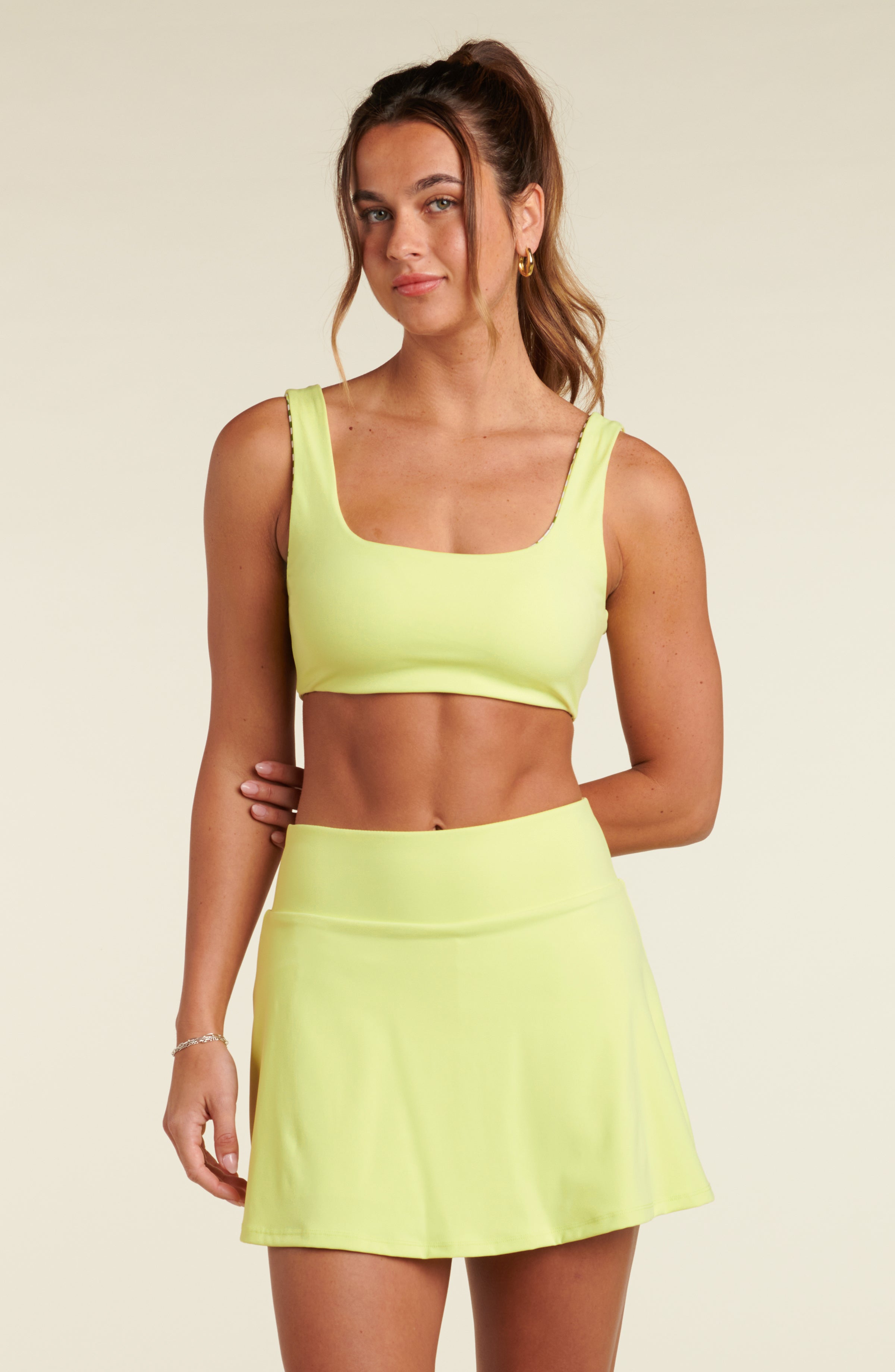 Woman wearing a lime green sports bra and matching swim skort against a white background.