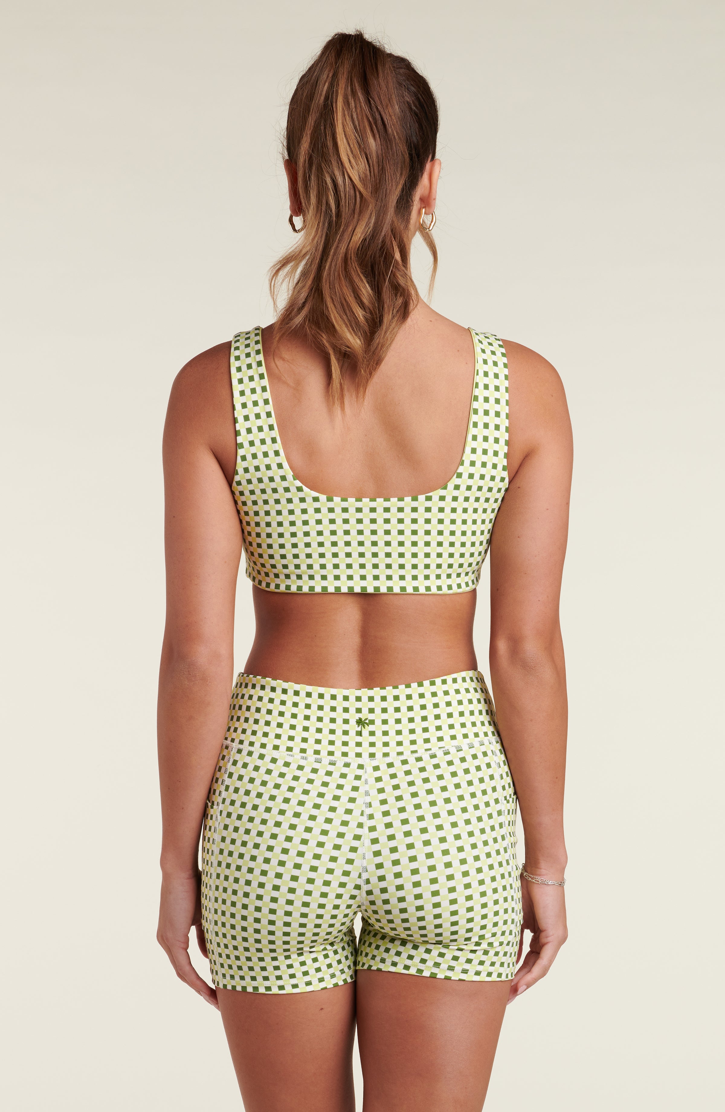 Woman wearing a green and white checkered sports bra and matching bike shorts against a white background.