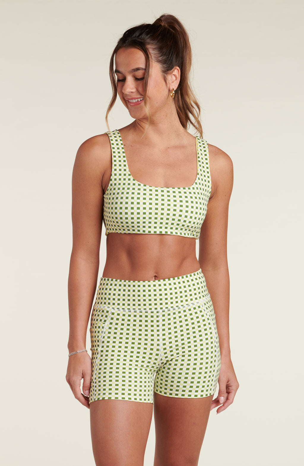 Woman wearing a green and white checkered sports bra and matching bike shorts against a white background.