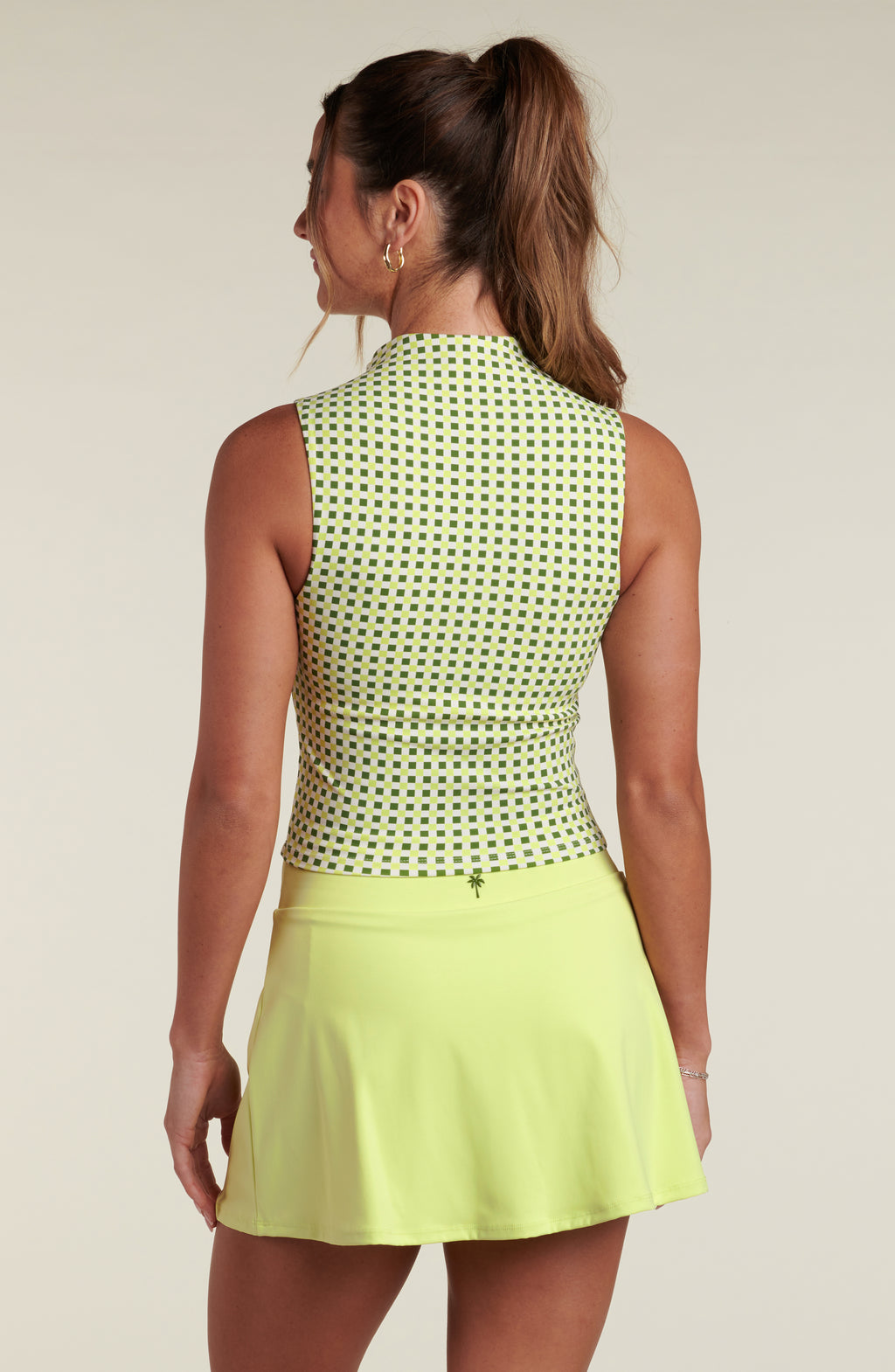 Woman wearing a green patterned sleeveless top and lime green skirt against a beige background. 