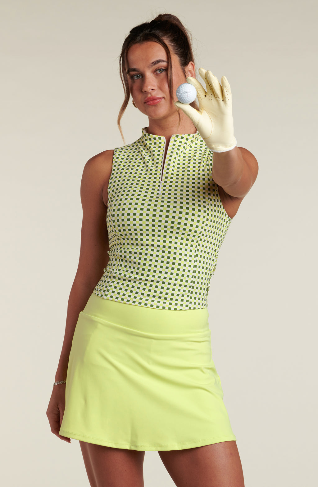 Woman wearing a green patterned sleeveless top and lime green skirt against a beige background. 