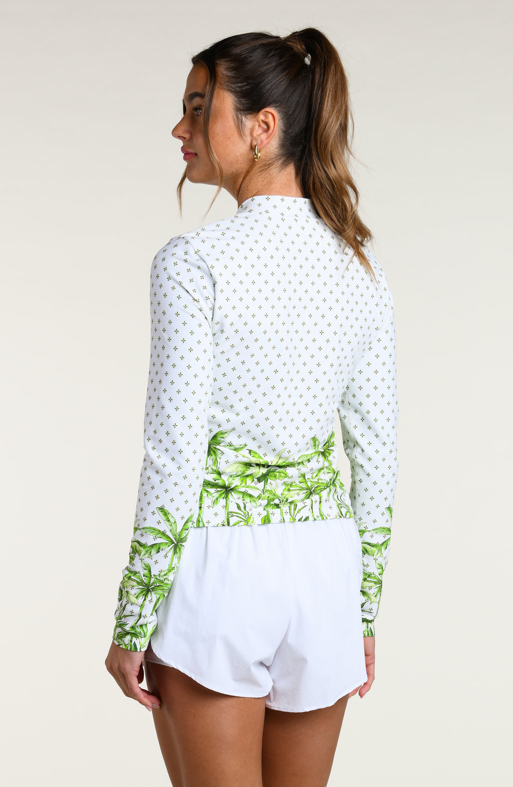 Woman wearing a white long-sleeve shirt with green palm tree design and white shorts on a plain background