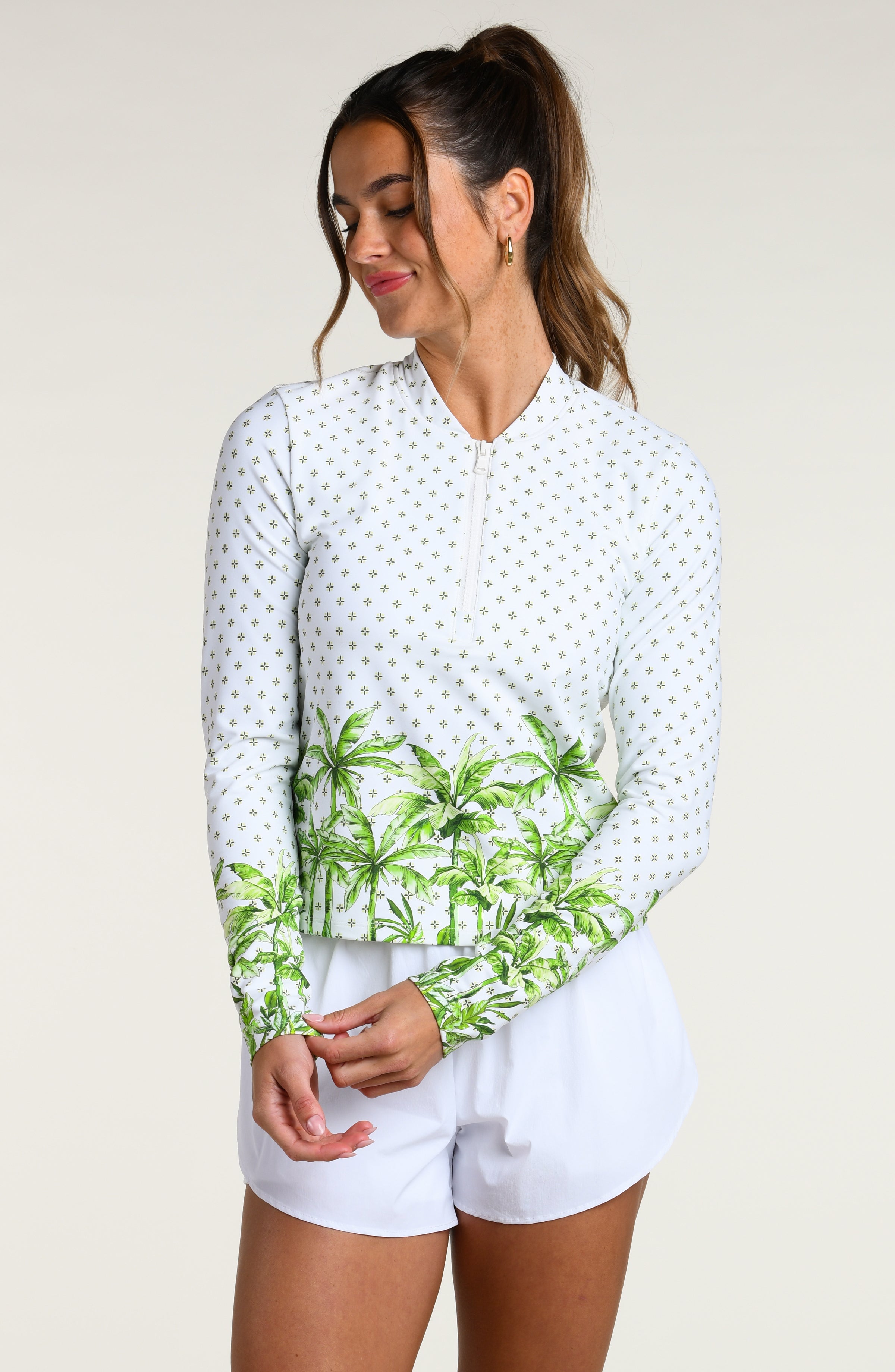 Woman wearing a white long-sleeve shirt with green palm tree design and white shorts on a plain background