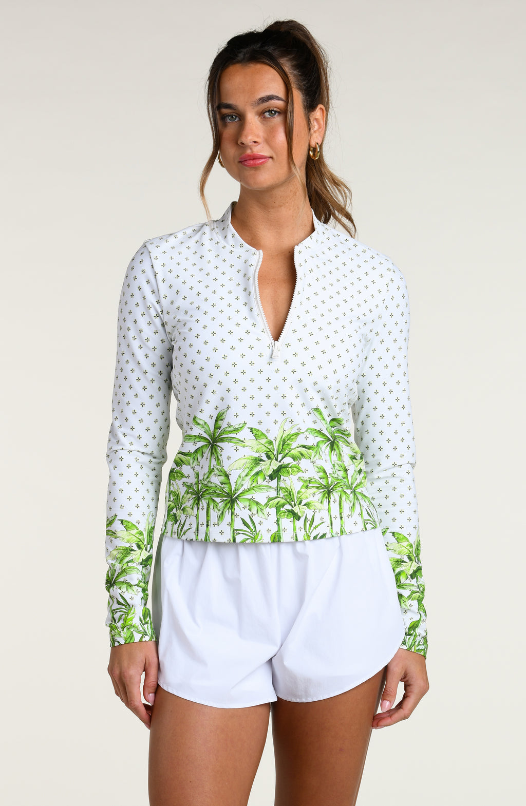 Woman wearing a white long-sleeve top with palm tree design and white shorts against a white background