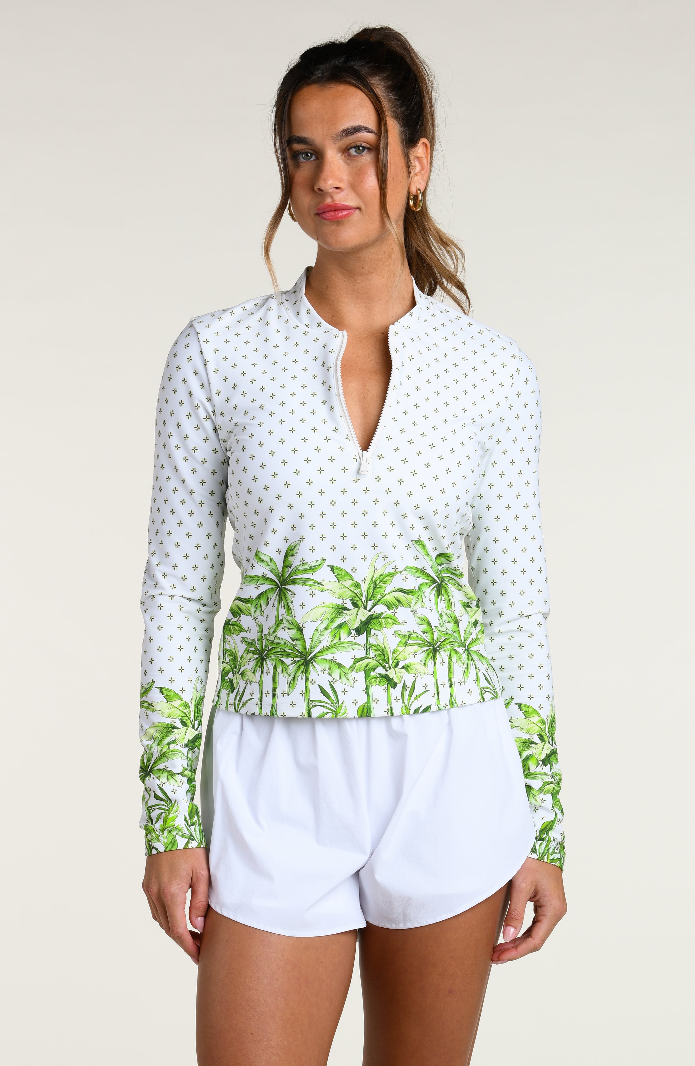 Woman wearing a white long-sleeve top with palm tree design and white shorts against a white background