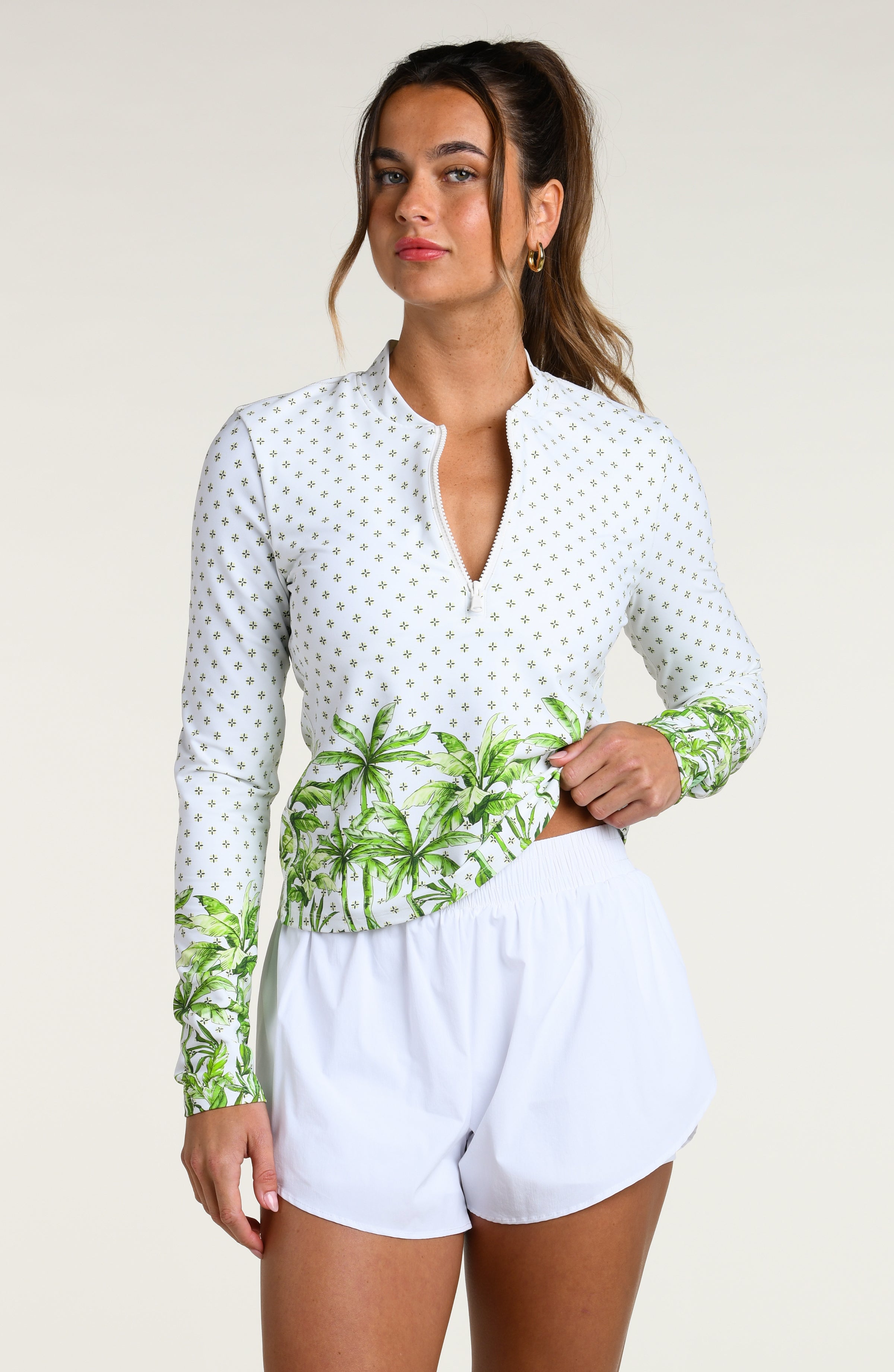 Woman wearing a white long-sleeve top with palm tree design and white shorts against a white background