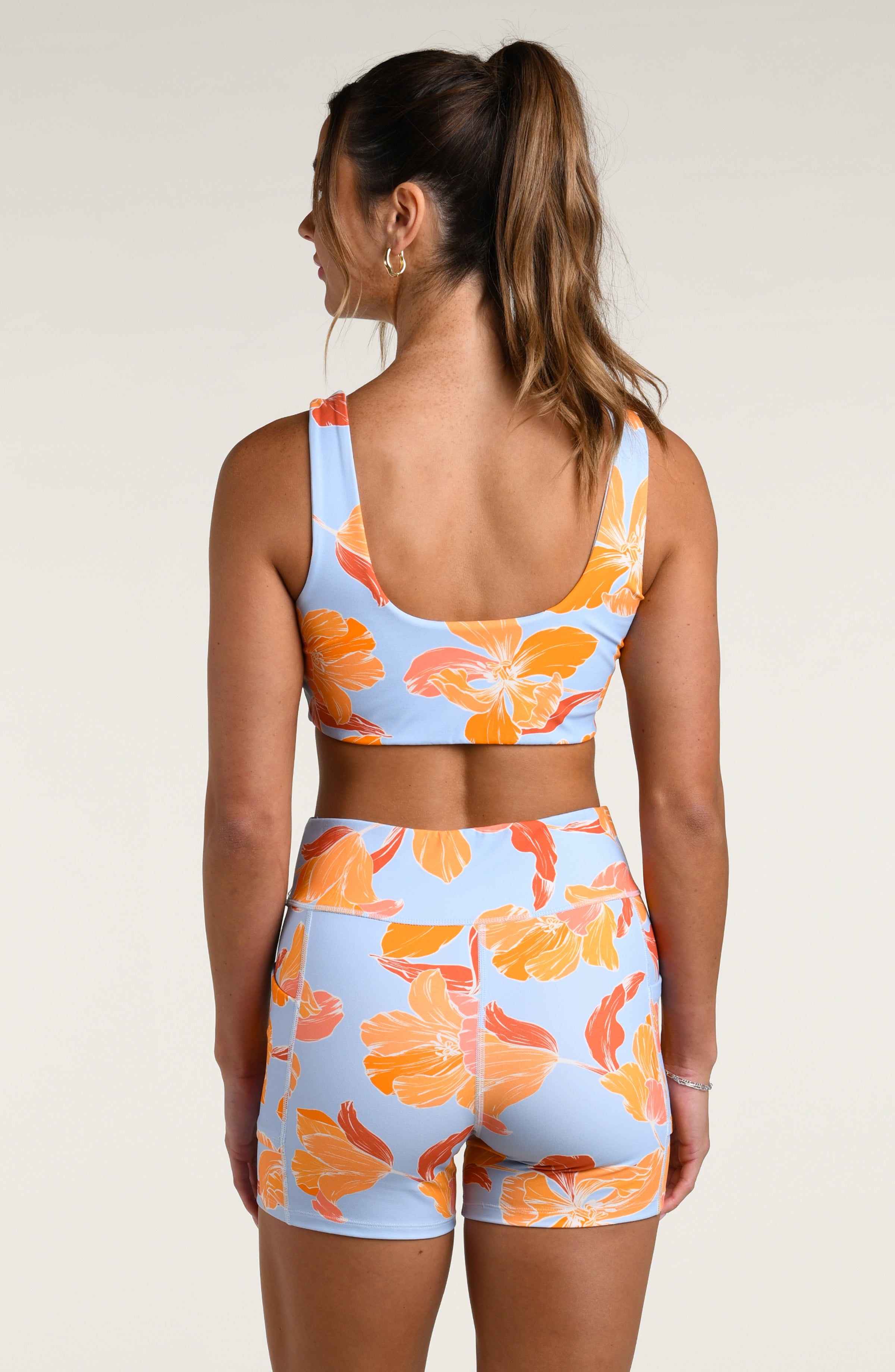 Woman wearing a floral patterned sports bra and matching biker shorts on a plain background