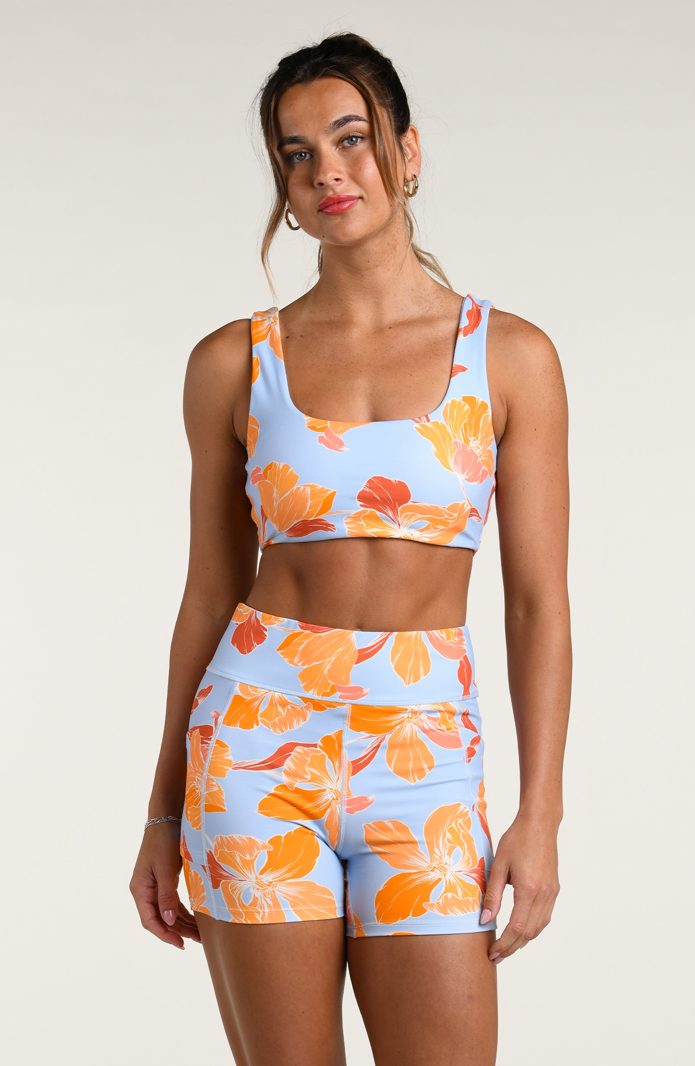 Woman wearing a floral patterned sports bra and matching biker shorts on a plain background