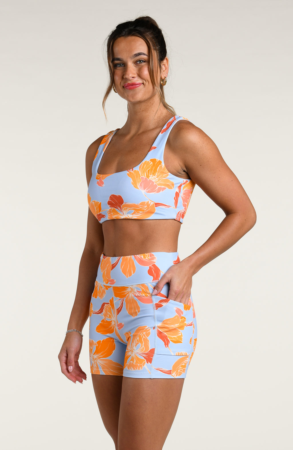 Woman wearing a floral patterned sports bra and matching biker shorts on a plain background