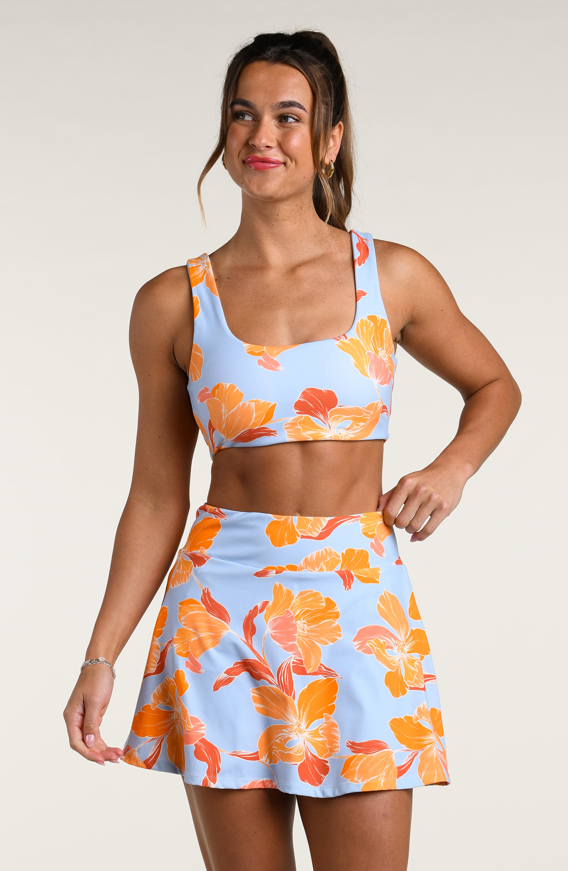 Woman wearing a floral reversible sports bra and matching skort on a plain background