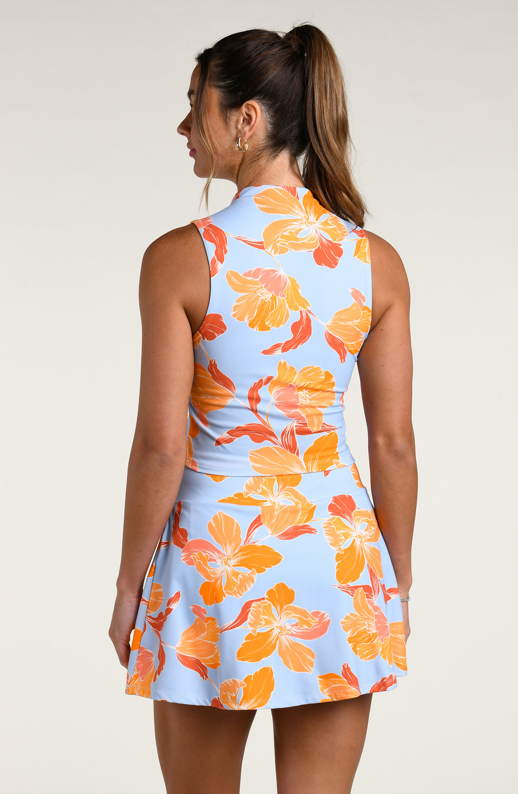 Woman wearing a sleeveless top and matching bottom with orange floral pattern on a light blue background