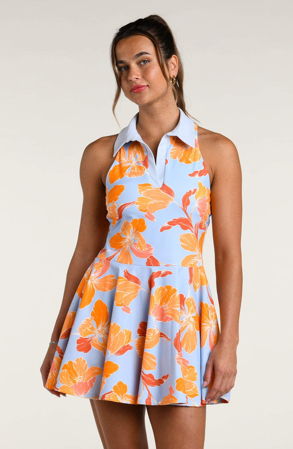 Woman wearing a floral tennis dress with orange flowers on a light blue background