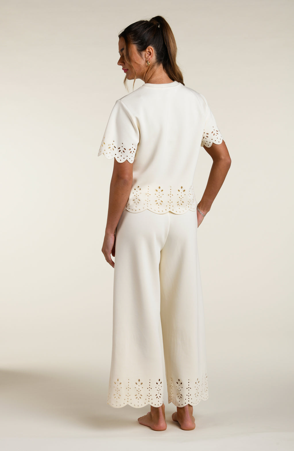 Woman wearing a beige short sleeve top with scalloped edges and matching pants on a plain background
