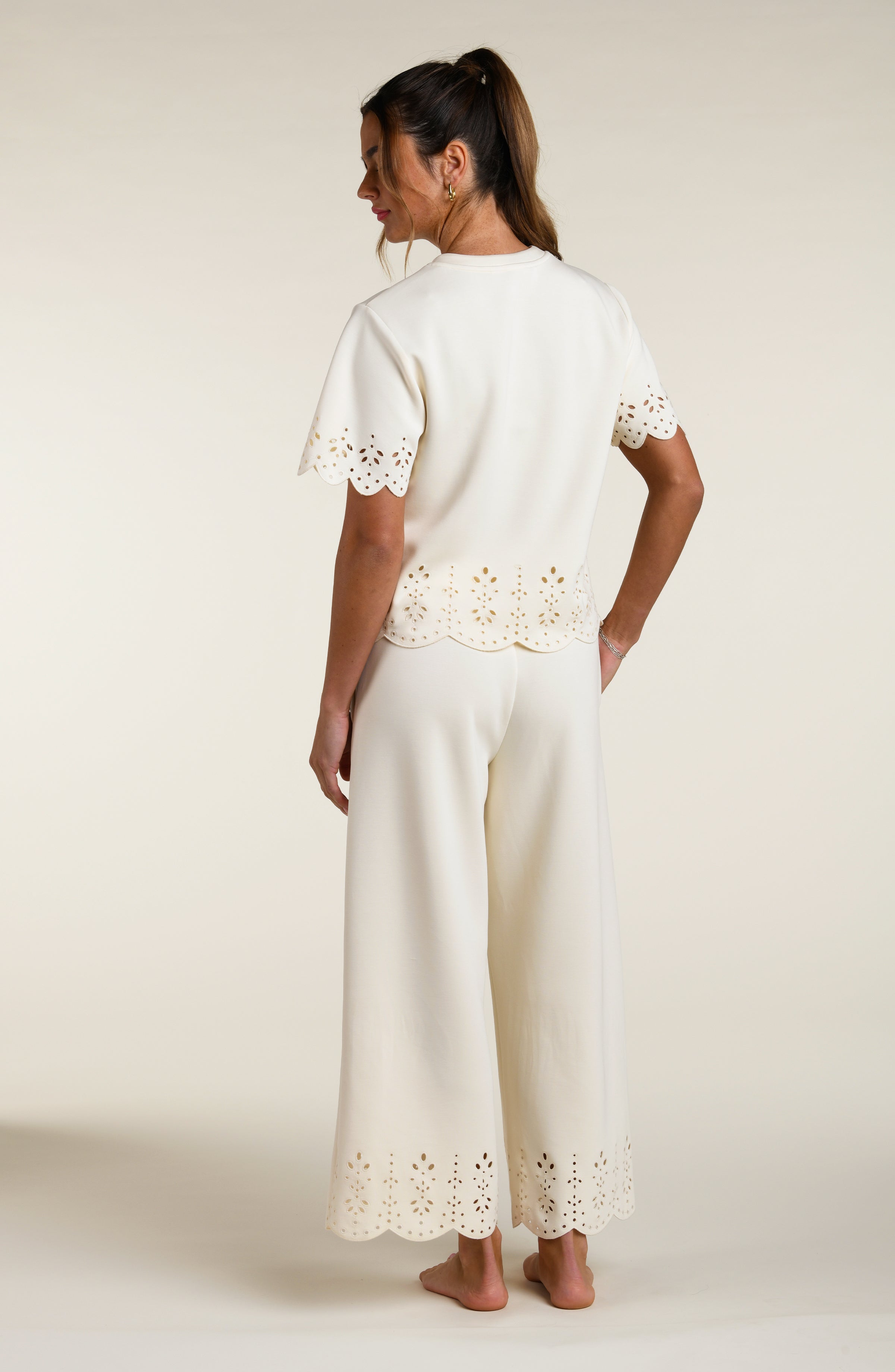 Woman wearing a beige short sleeve top with scalloped edges and matching pants on a plain background