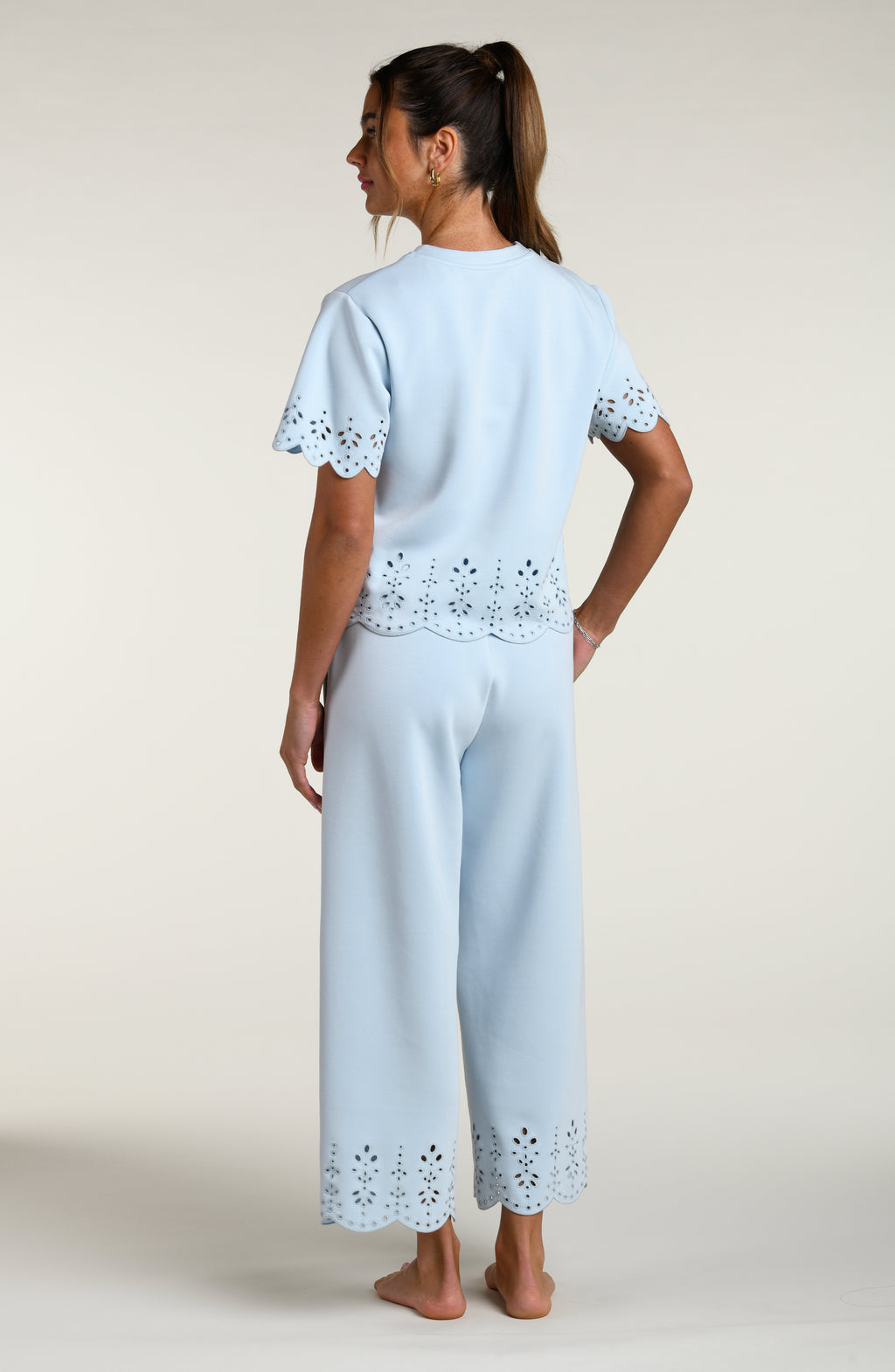 Woman wearing a light blue short sleeve top with scalloped edges and a matching pants on a plain background