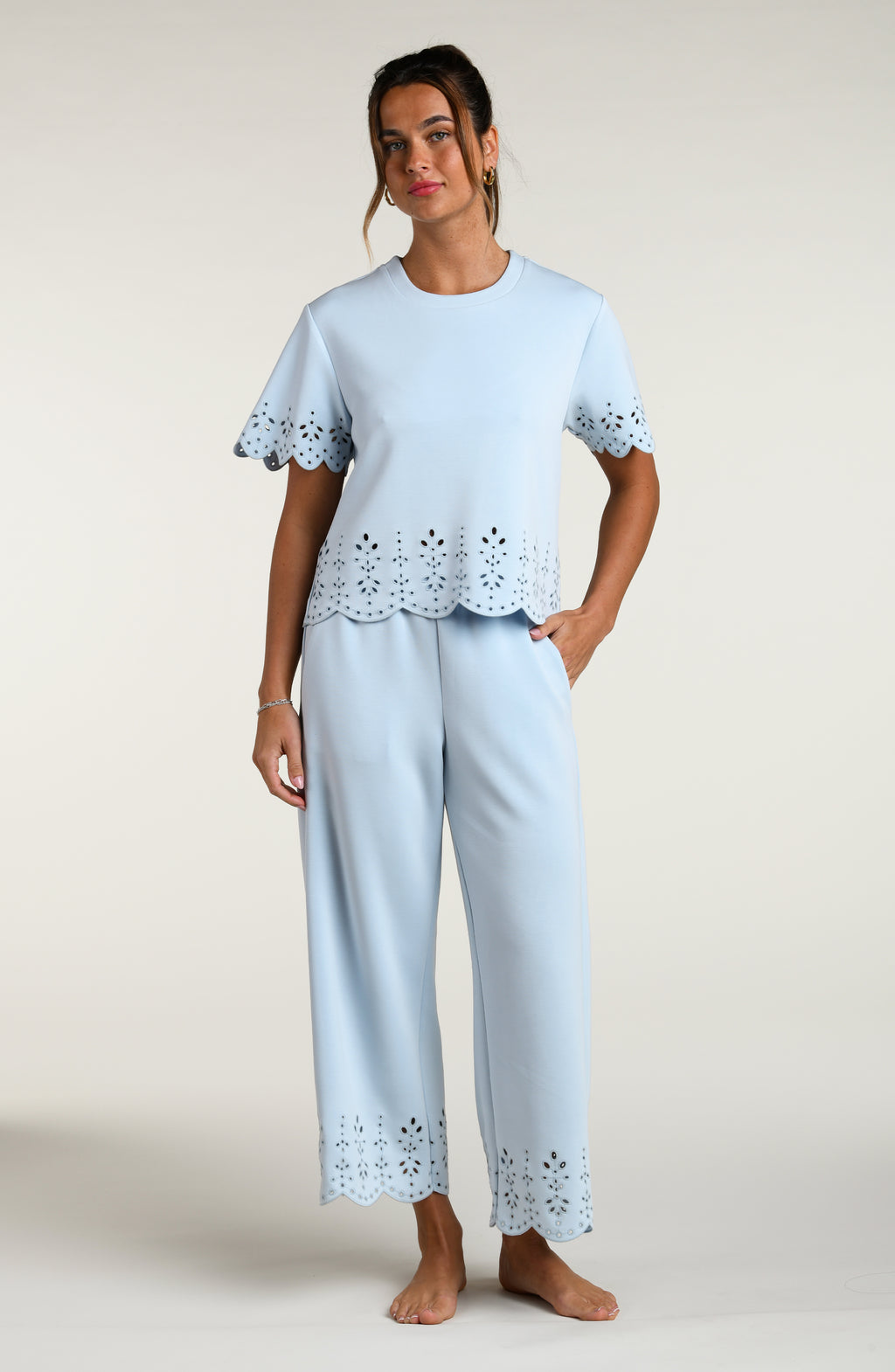 Woman wearing a light blue short sleeve top with scalloped edges and matching pants on a plain background