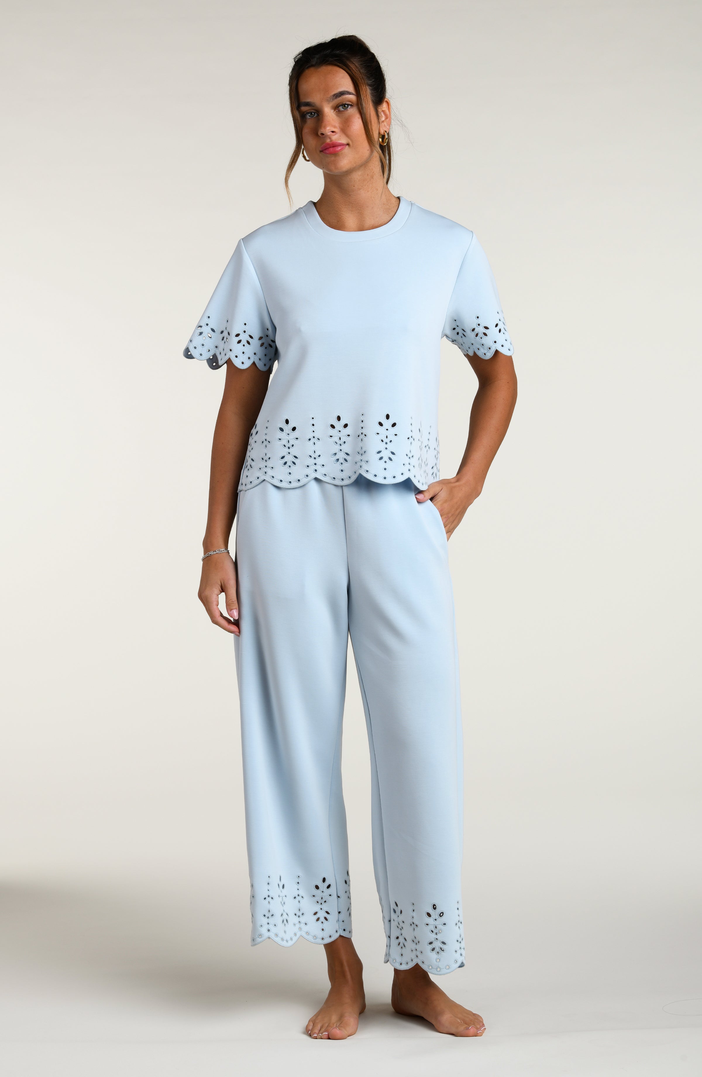 Woman wearing a light blue short sleeve top with scalloped edges and matching pants on a plain background