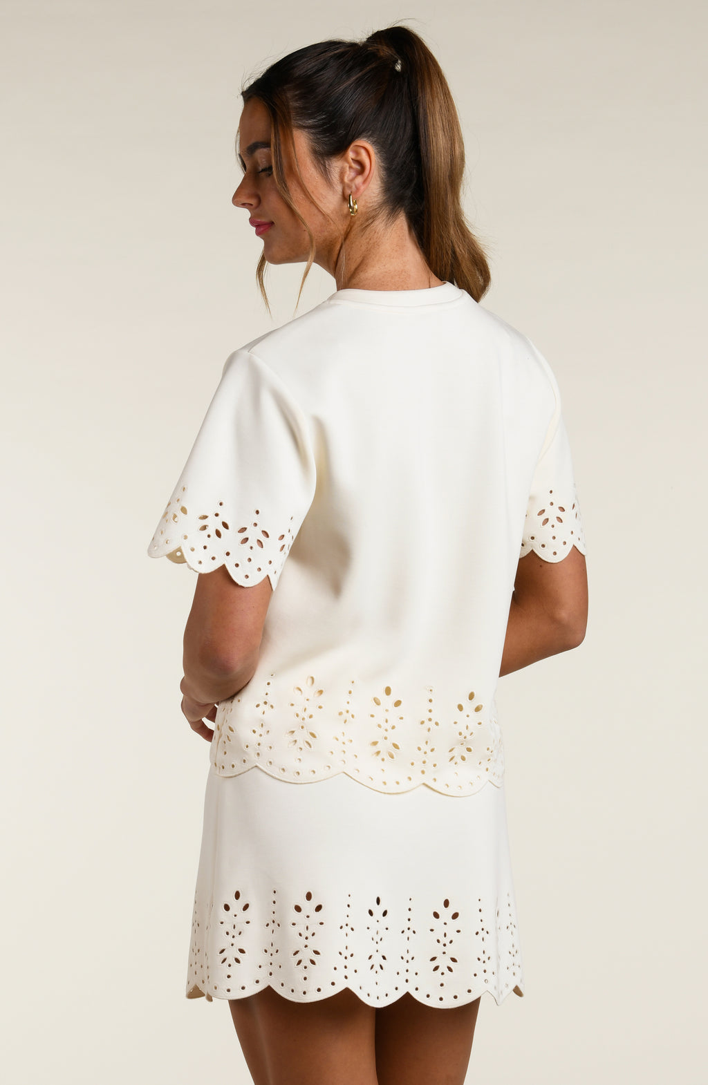 Woman wearing a beige short sleeve top with scalloped edges and a matching skirt on a plain background
