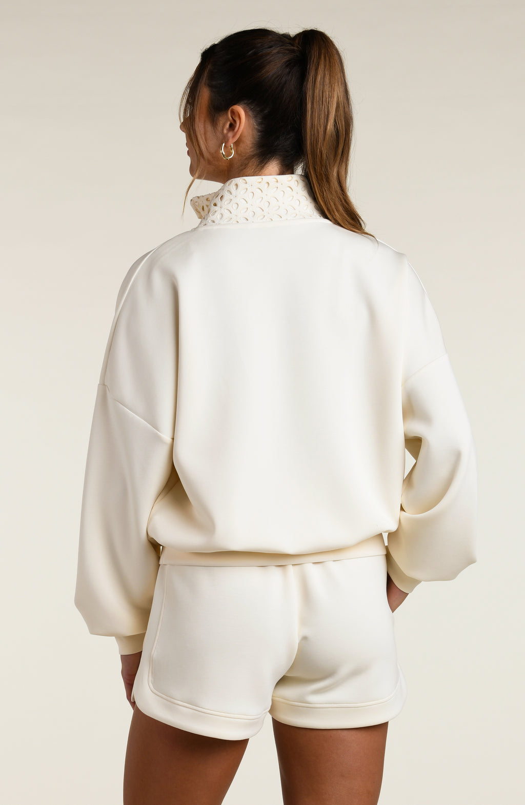 Woman wearing a cream-colored sweatshirt with a high-neck top and shorts on a plain background