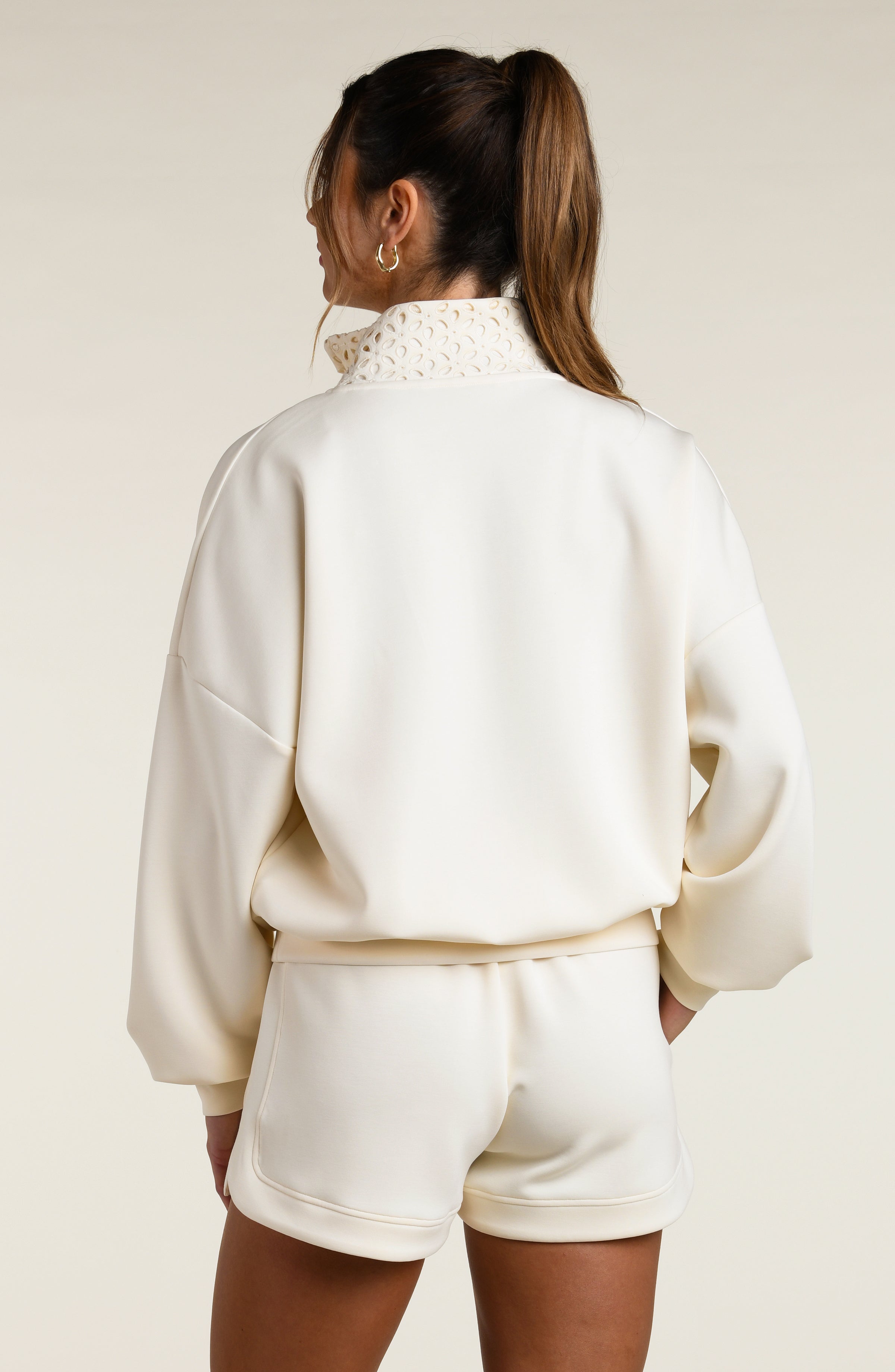 Woman wearing a cream-colored sweatshirt with a high-neck top and shorts on a plain background