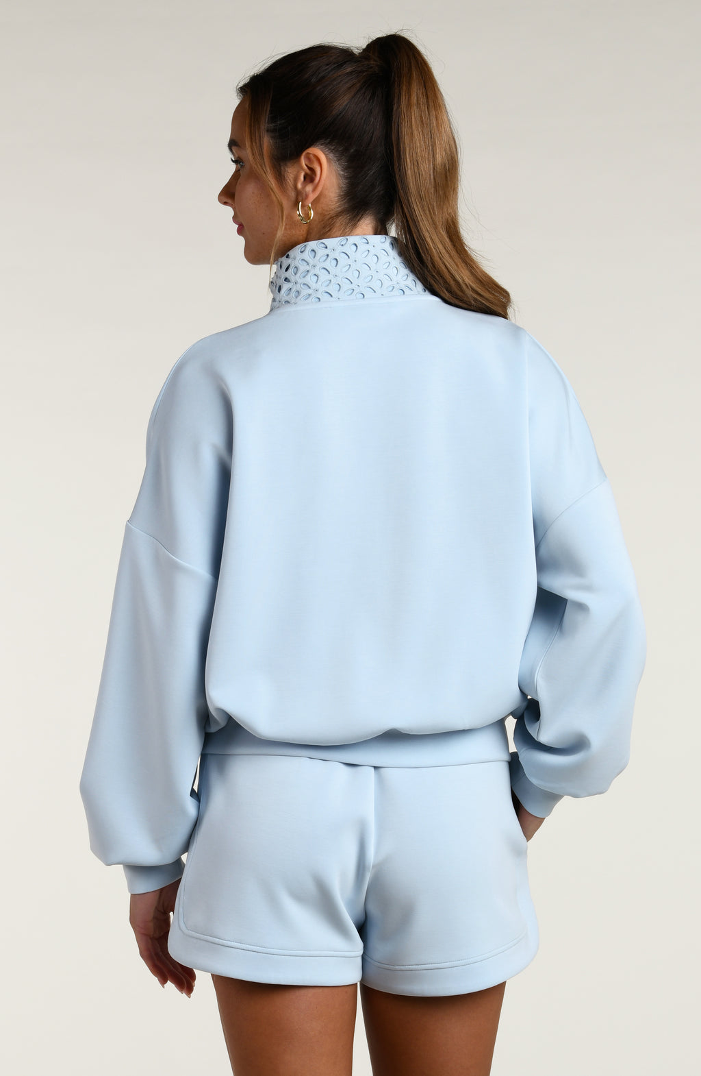 Woman wearing a light blue pullover with lace detailing and matching shorts on a beige background