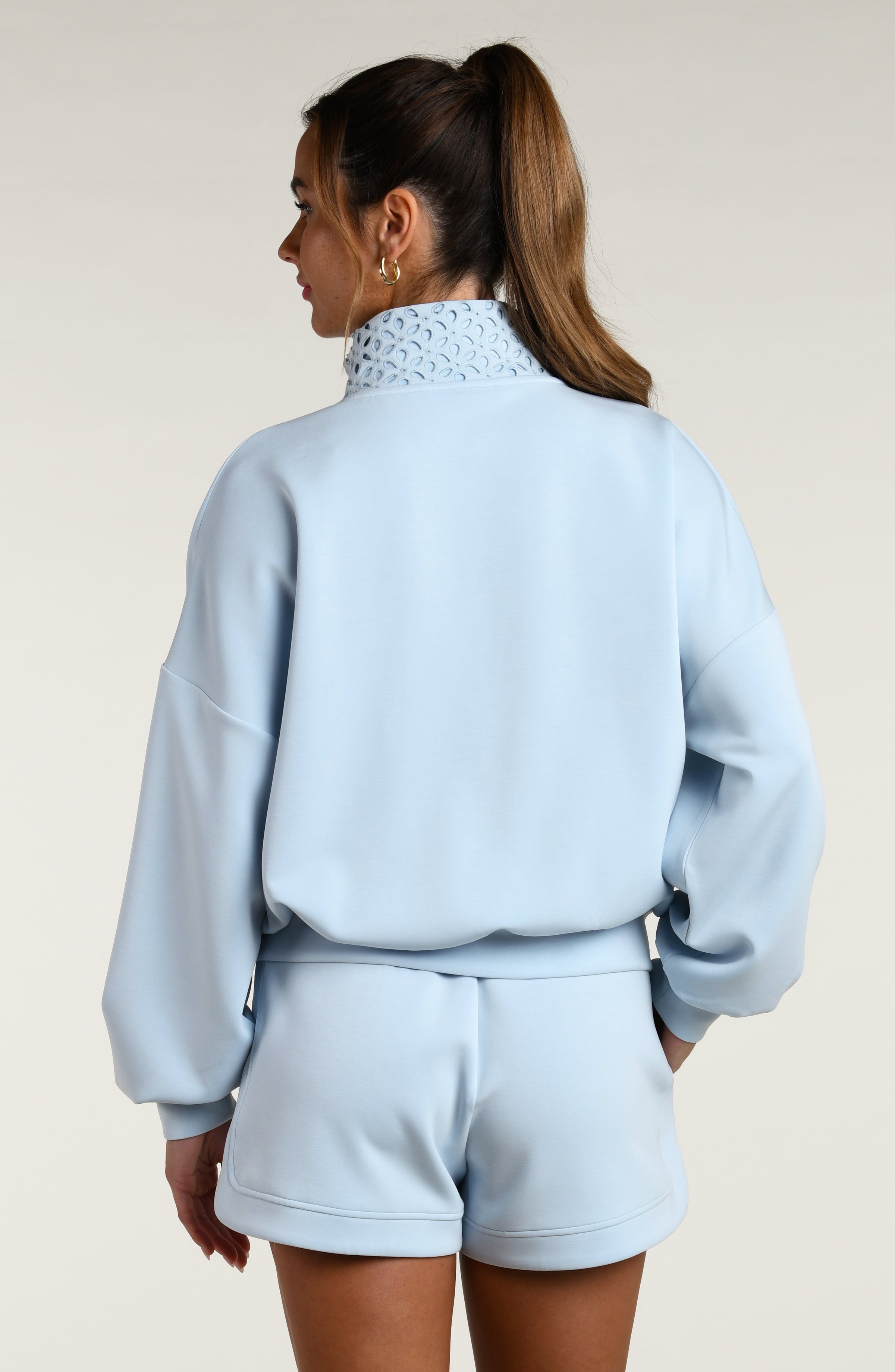 Woman wearing a light blue pullover with lace detailing and matching shorts on a beige background