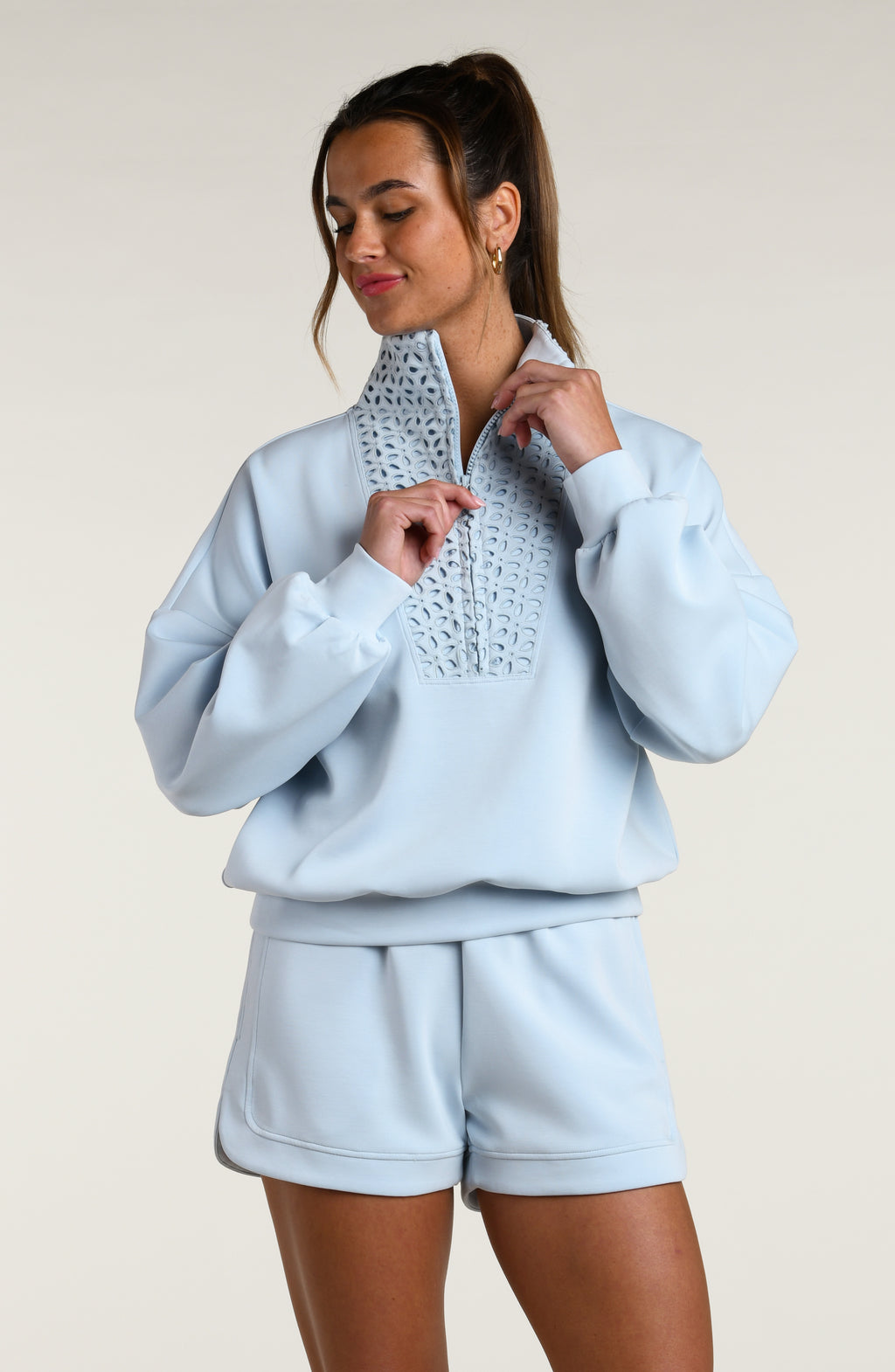 Woman wearing a light blue pullover with lace detailing and matching shorts on a beige background