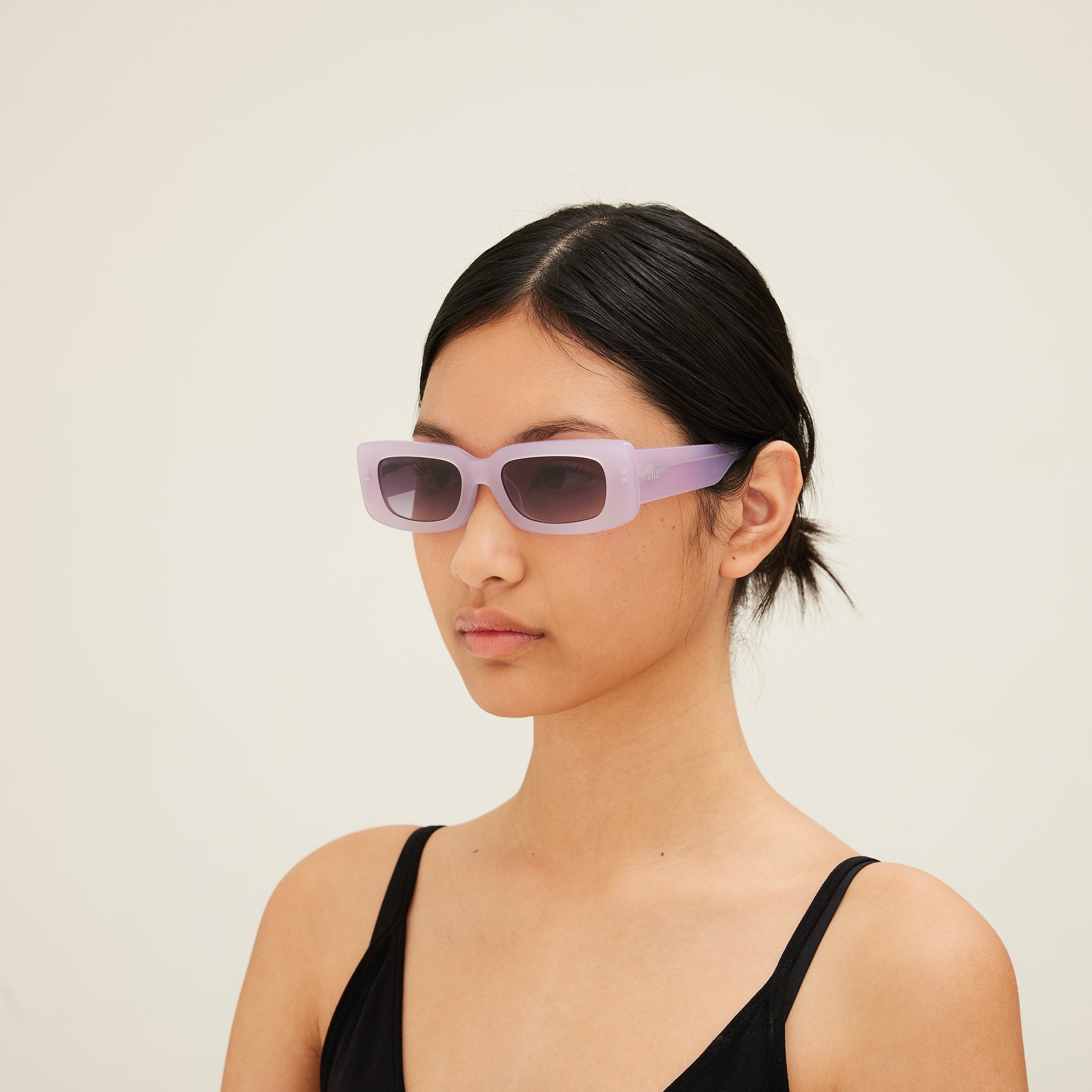 Woman wearing pink sunglasses with dark lenses on a white background