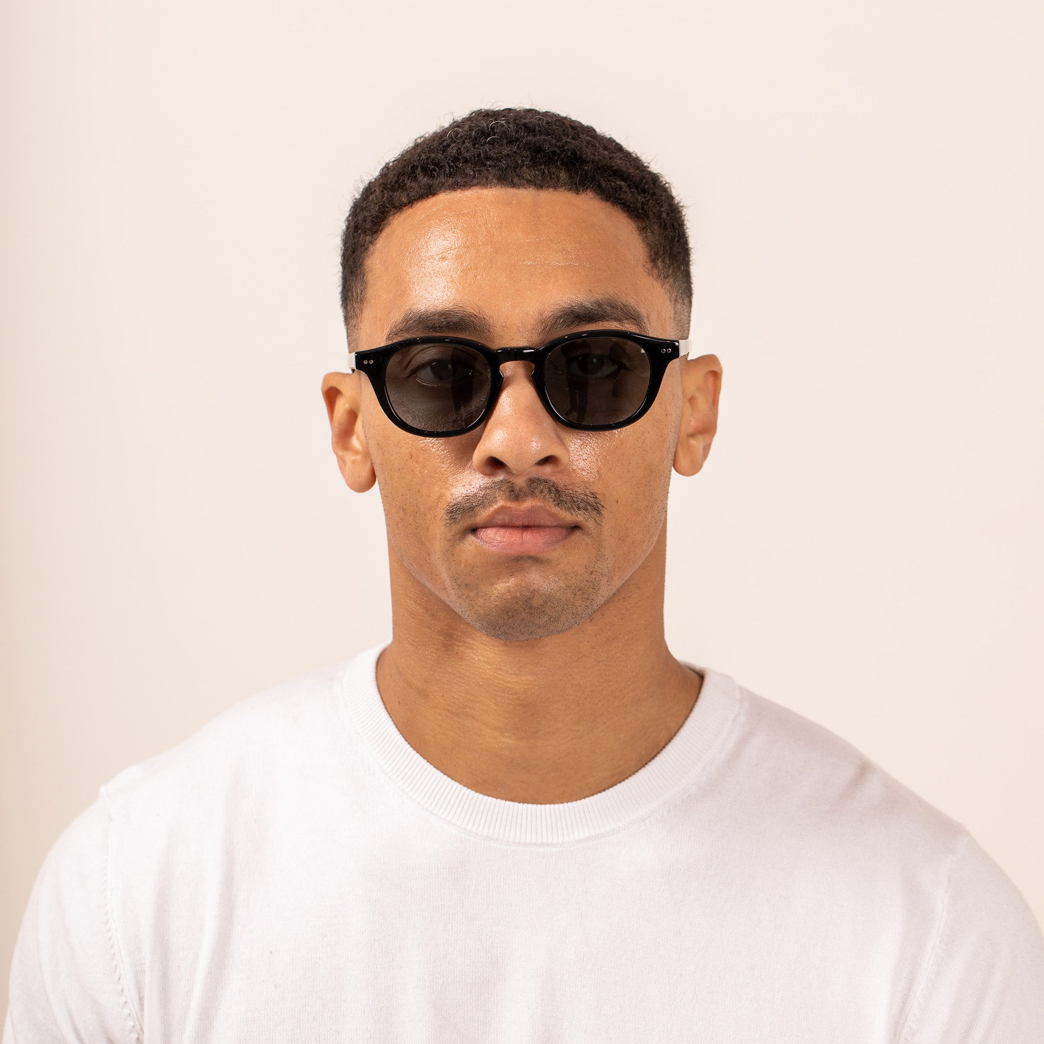 Man wearing black sunglasses and a white shirt against a beige background