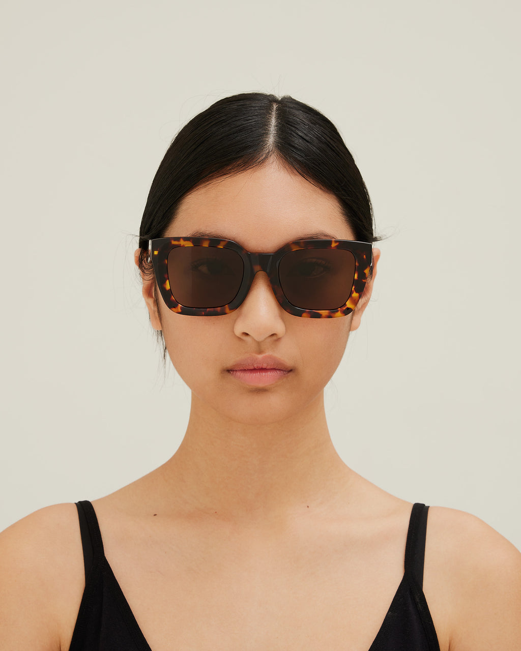 Woman wearing sunglasses with tortoiseshell frame and brown lenses on a white background