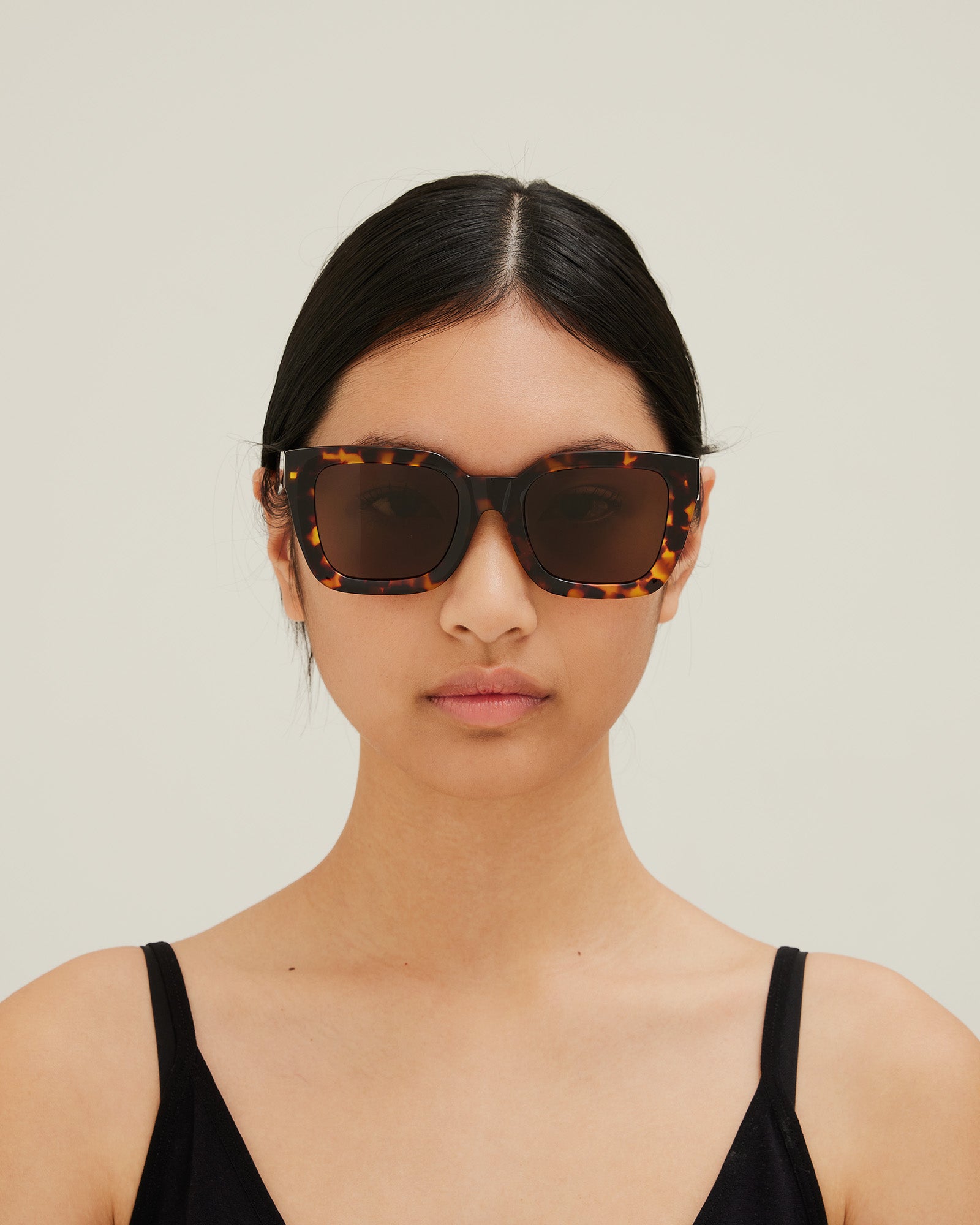 Woman wearing sunglasses with tortoiseshell frame and brown lenses on a white background