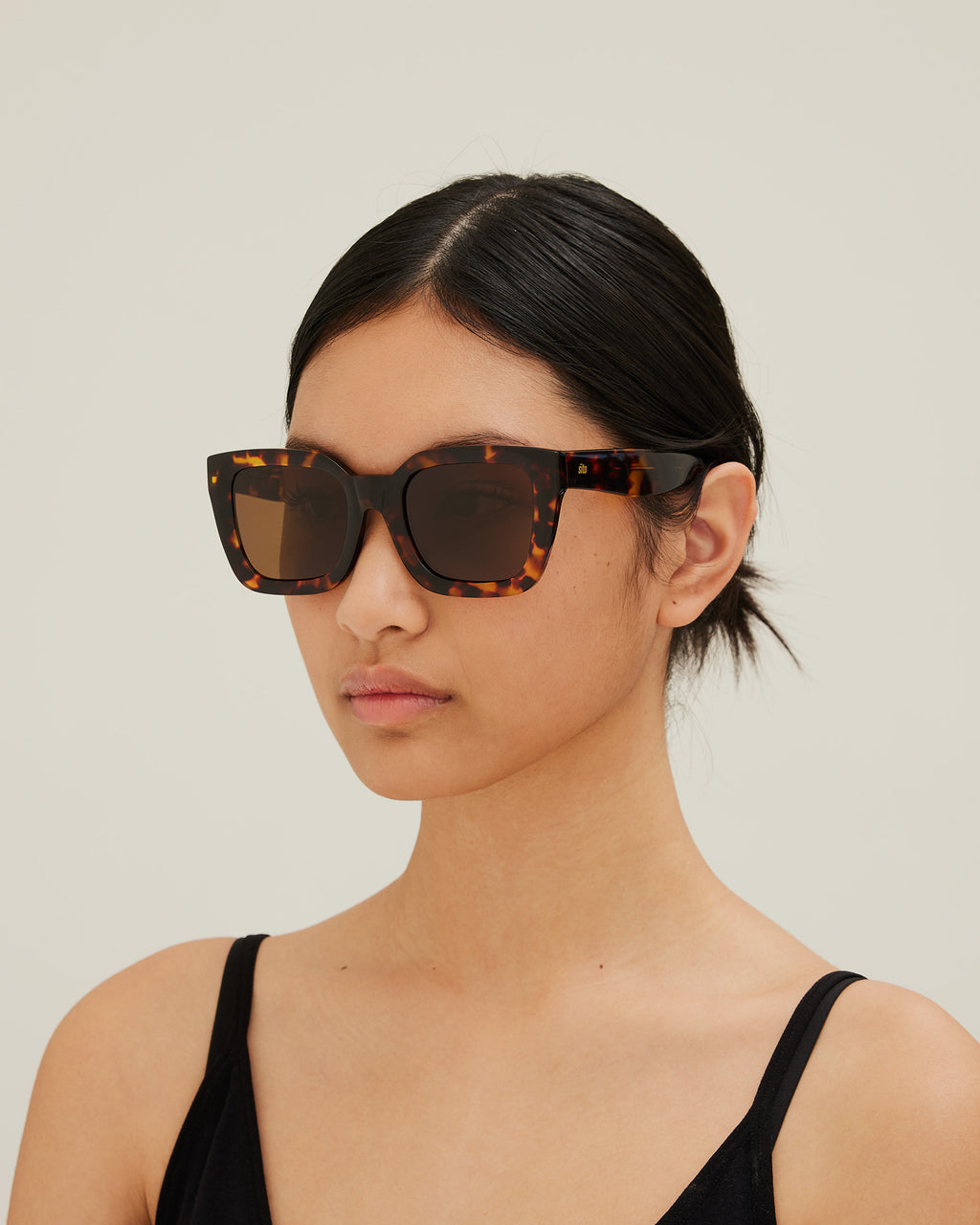 Woman wearing sunglasses with tortoiseshell frame and brown lenses on a white background