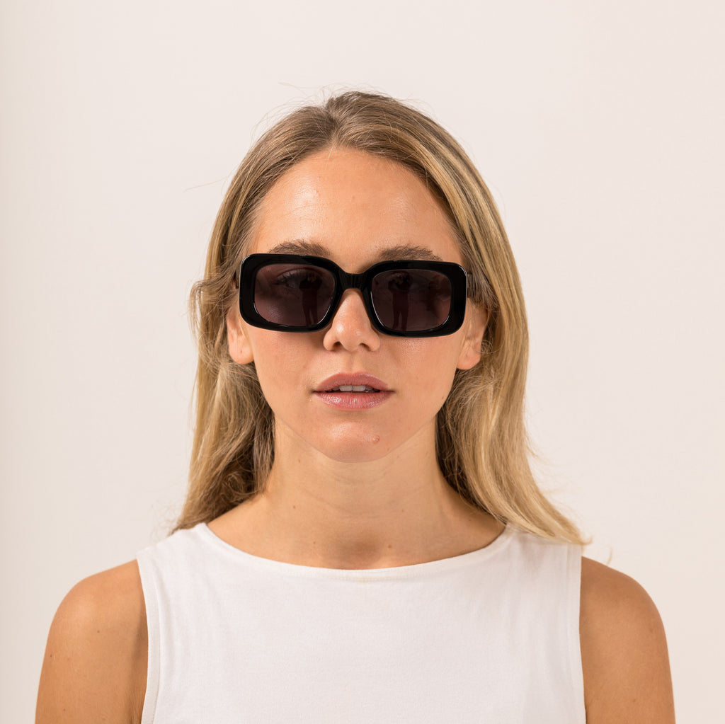 Woman wearing black sunglasses with gray lenses on a white background