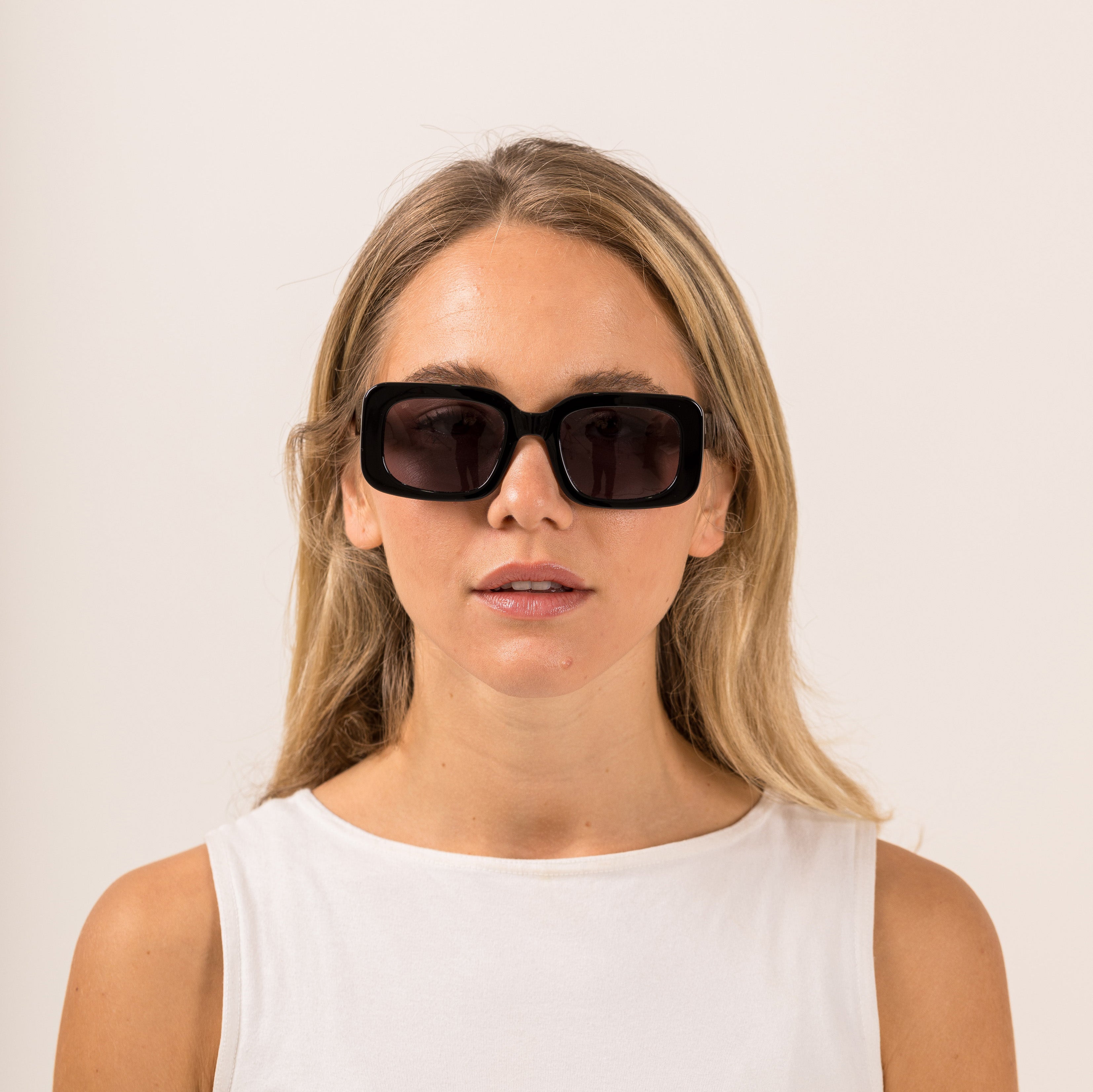 Woman wearing black sunglasses with gray lenses on a white background