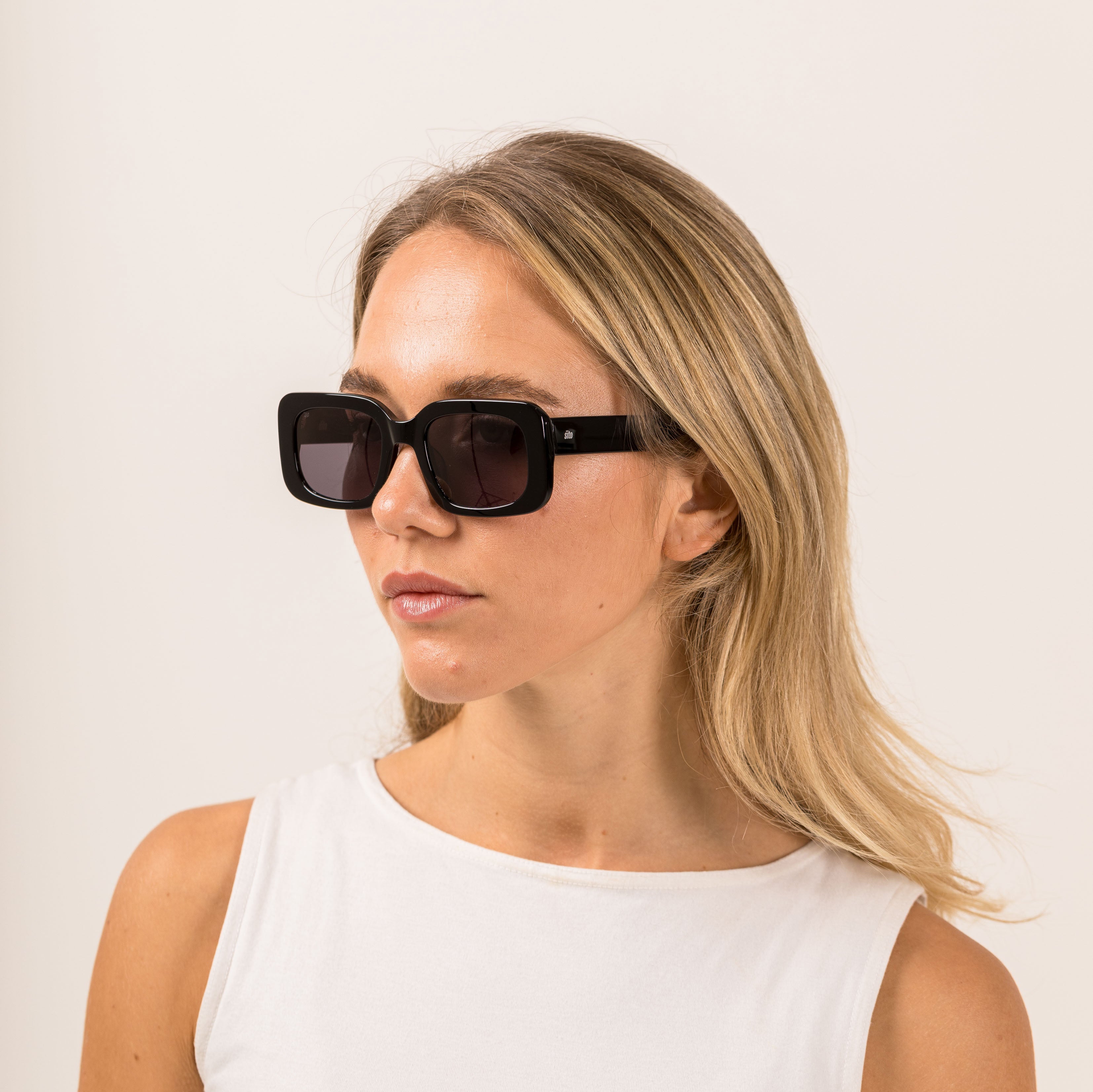 Woman wearing black sunglasses with gray lenses on a white background