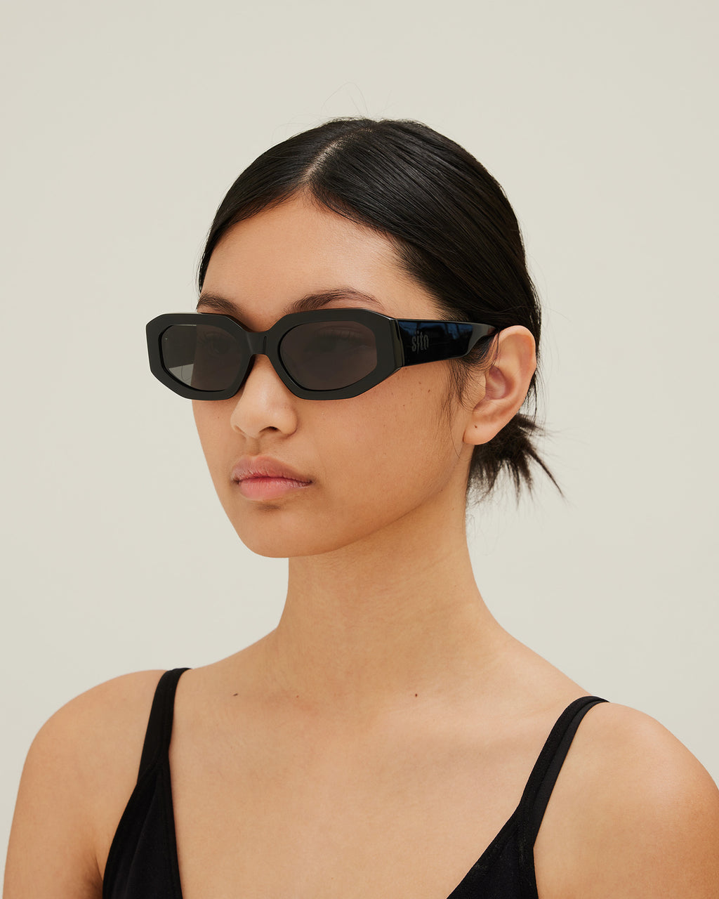 Woman wearing black sunglasses with gray lenses on a white background