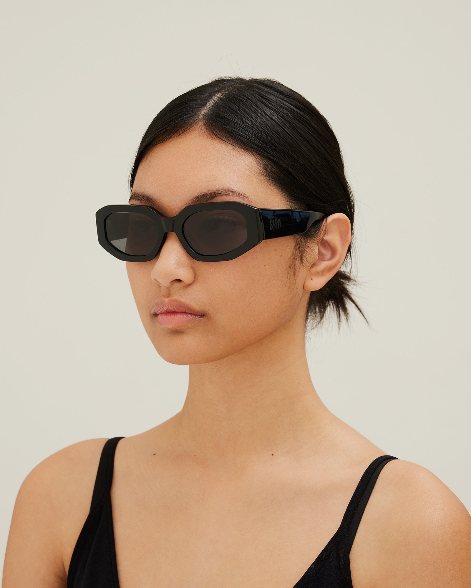 Woman wearing black sunglasses with gray lenses on a white background