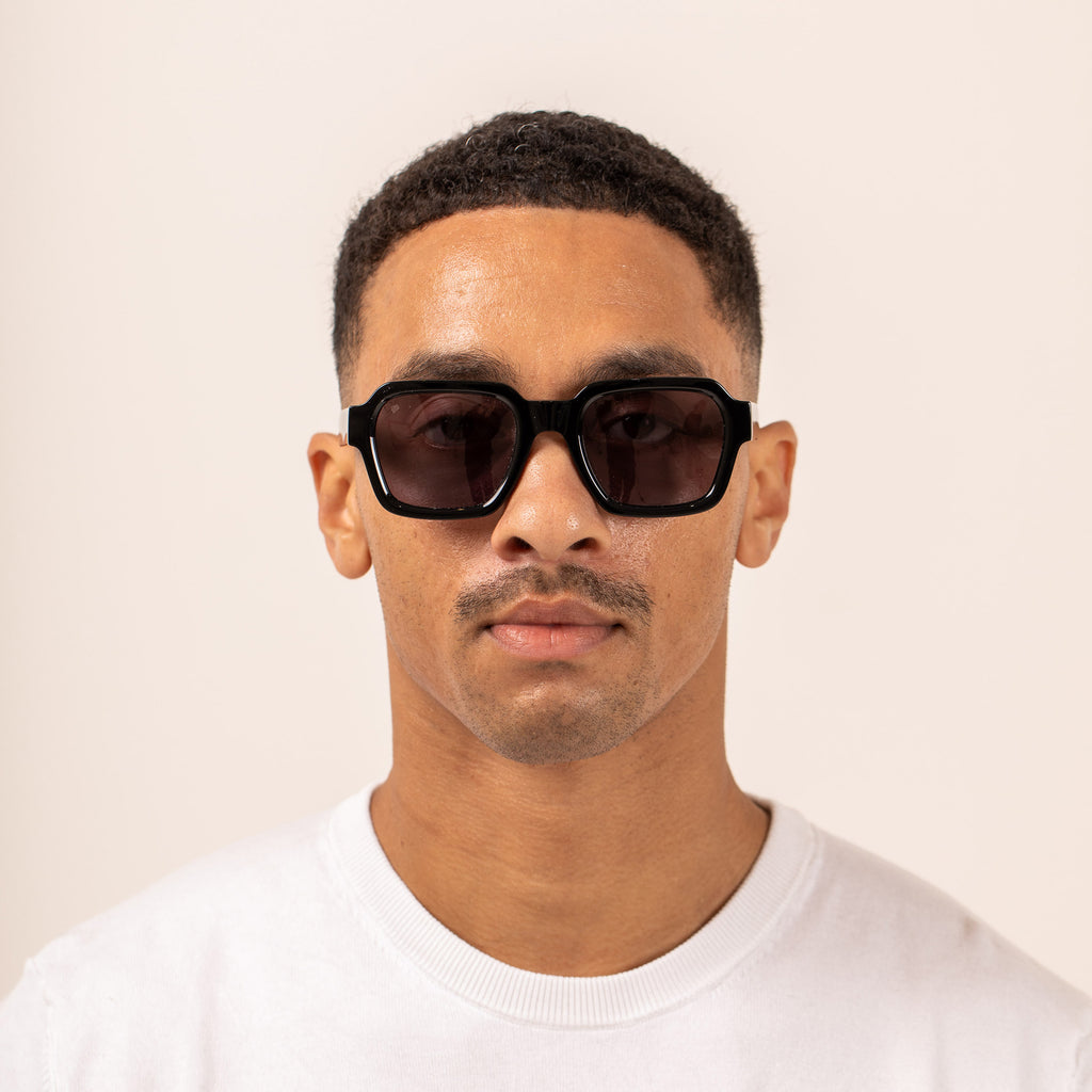 Man wearing black sunglasses and a white shirt against a beige background