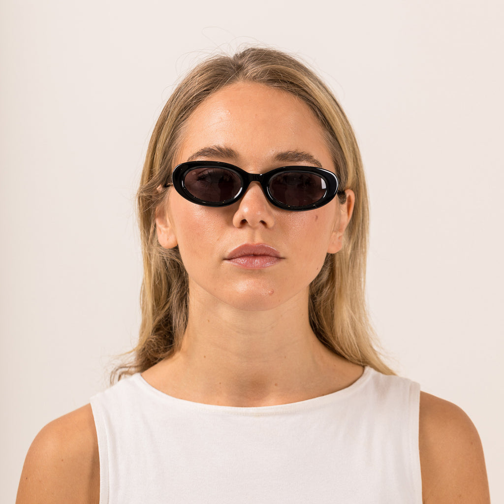 Woman wearing back sunglasses with purple lenses on a white background. 