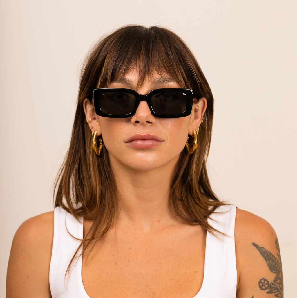 A woman wearing black sunglasses with gray lenses on a white background