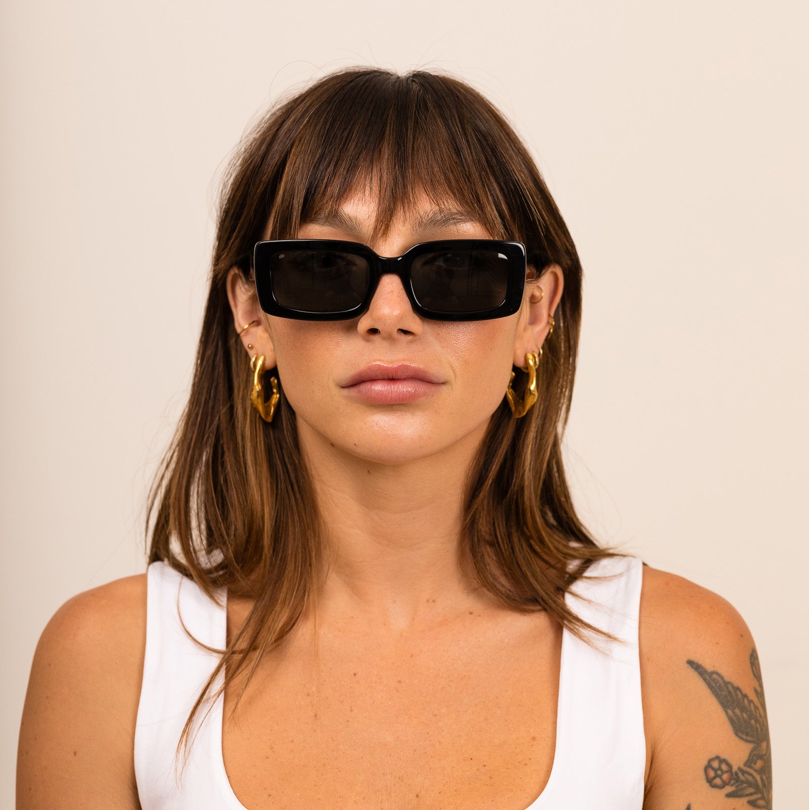 A woman wearing black sunglasses with gray lenses on a white background