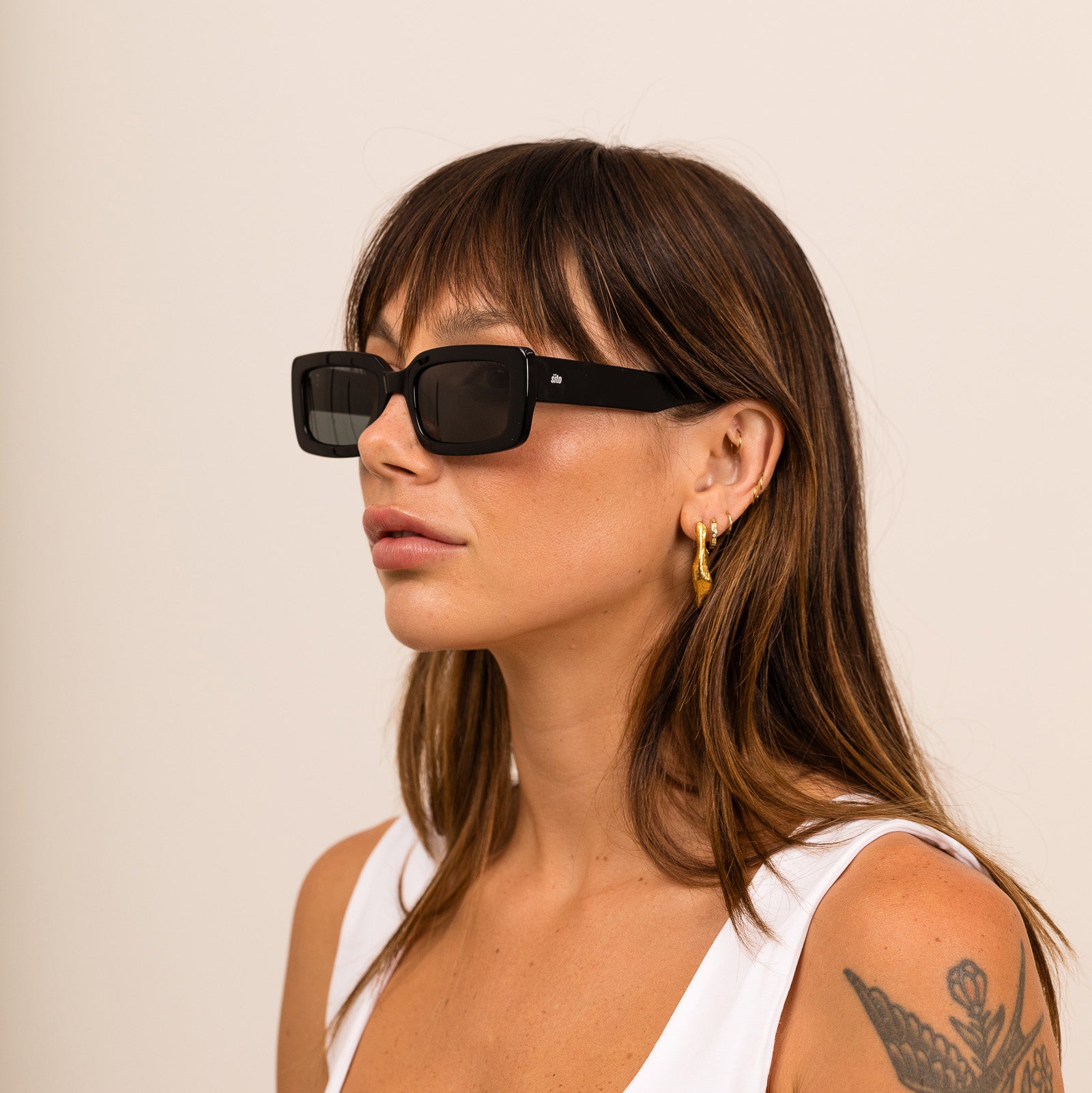 A woman wearing black sunglasses with gray lenses on a white background