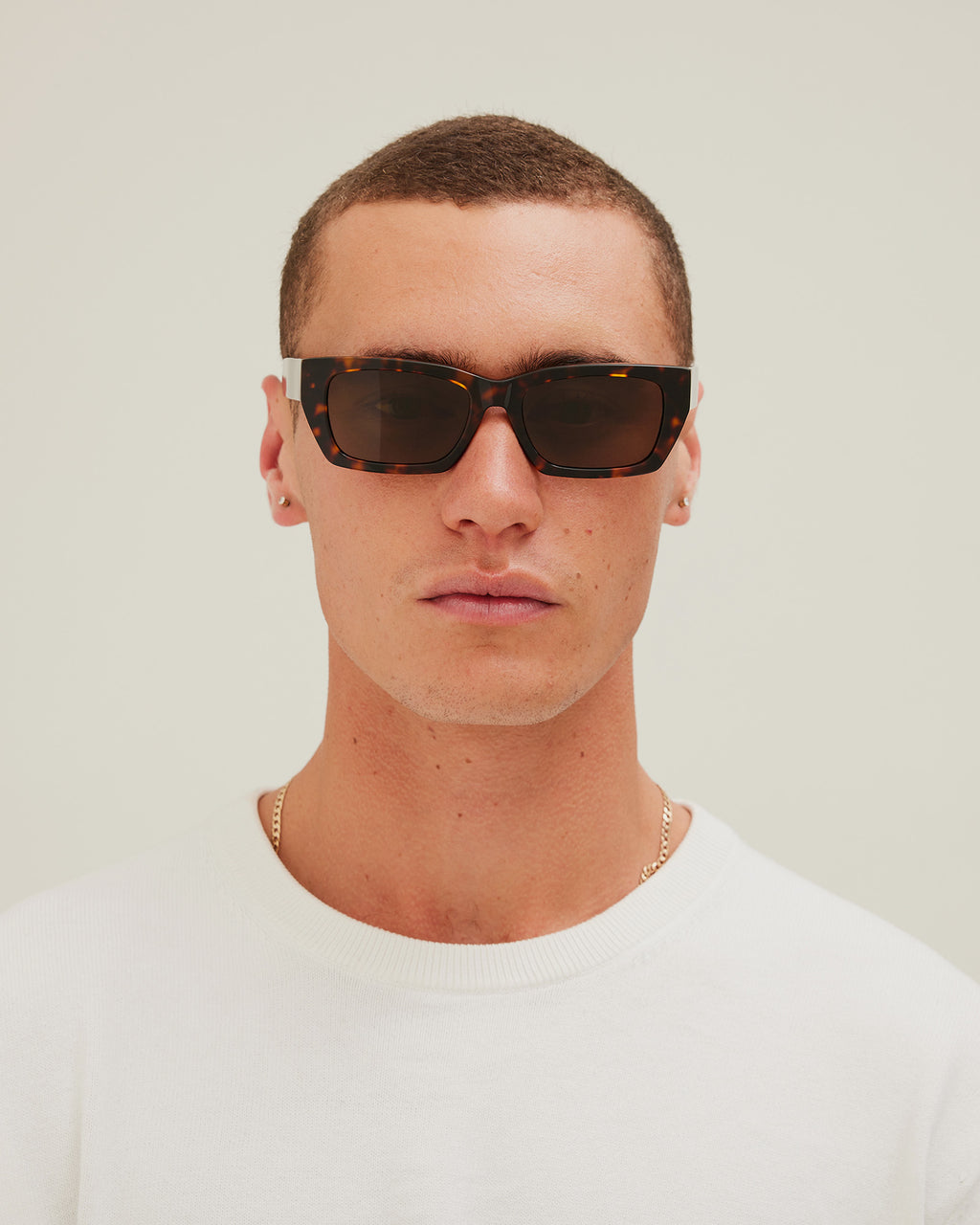 Man wearing sunglasses with tortoiseshell frame and brown lenses on a white background