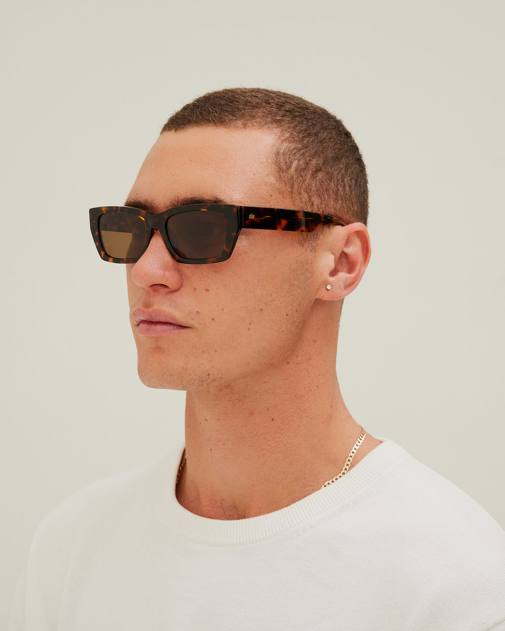 Man wearing sunglasses with tortoiseshell frame and brown lenses on a white background