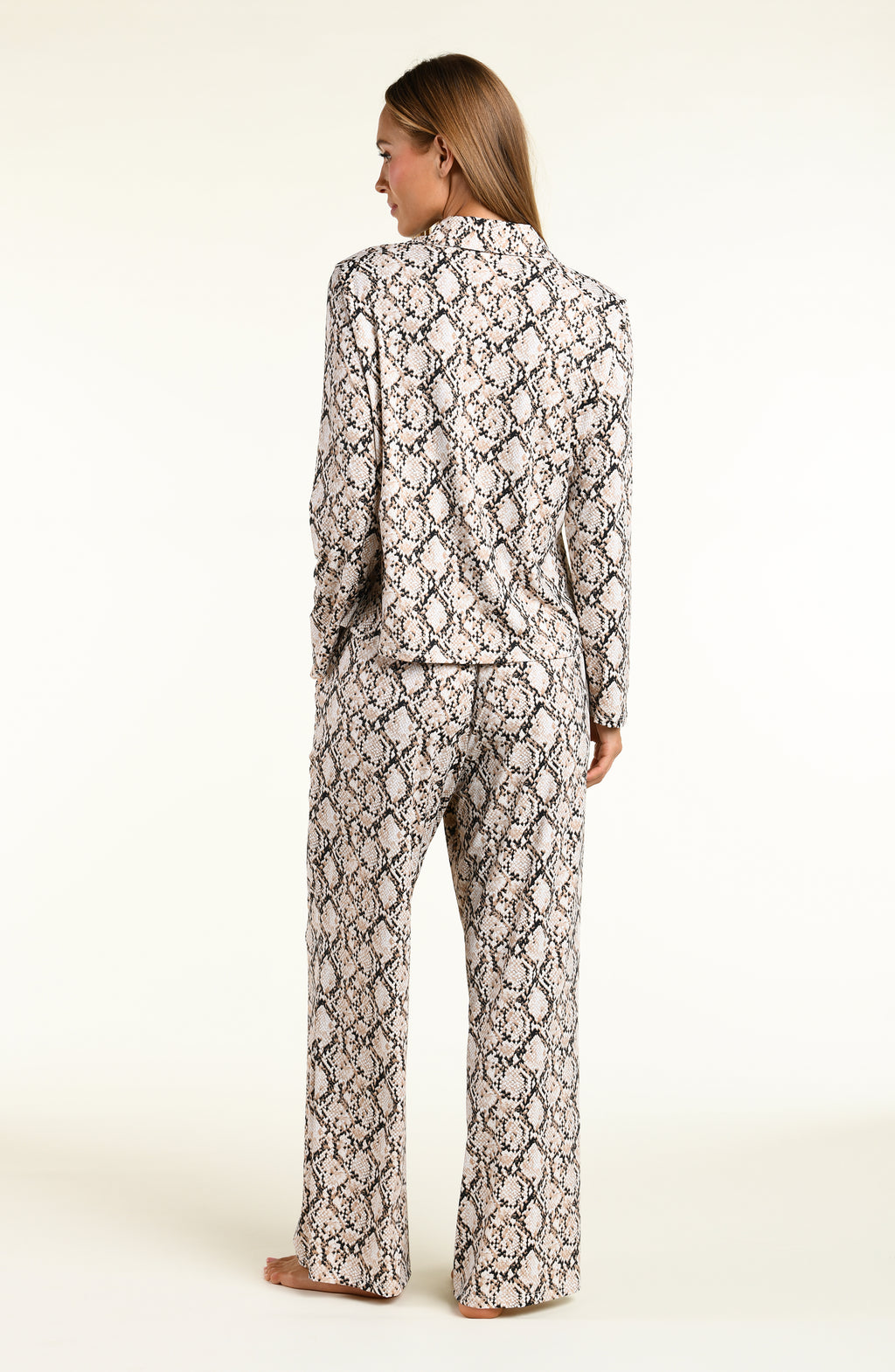 A woman shown from the back wearing a matching long-sleeve top and wide-leg pants set in a beige, black, and white snakeskin pattern, set against a plain off-white studio background.